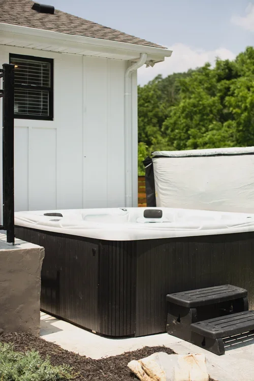 Hot tub outside the Villa at Ramble Creek, featuring a private patio setting, black exterior, steps, and greenery surrounding the outdoor space.