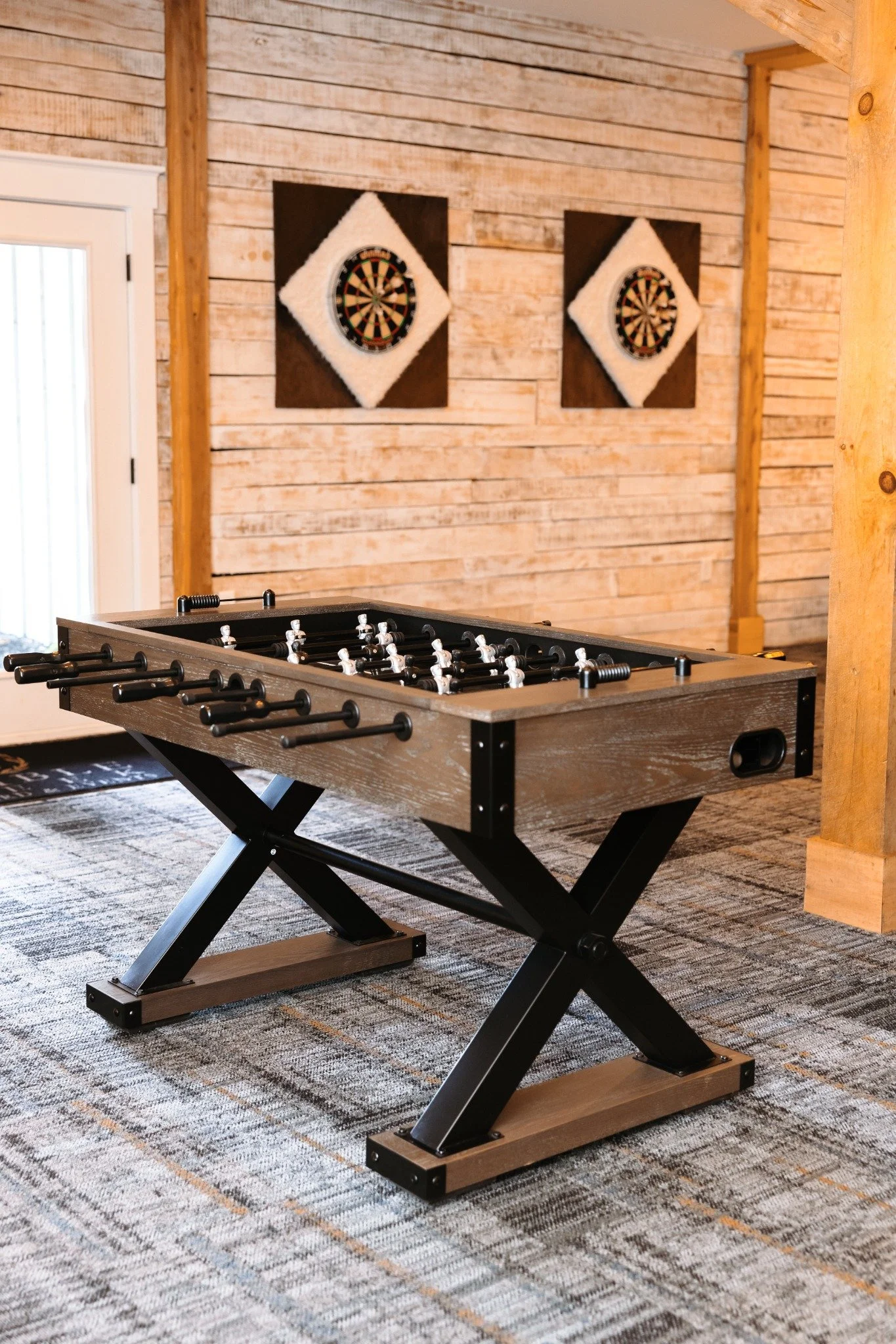 A foosball table in a groom's quarters with wooden walls and two dartboards hanging on the wall behind it.
