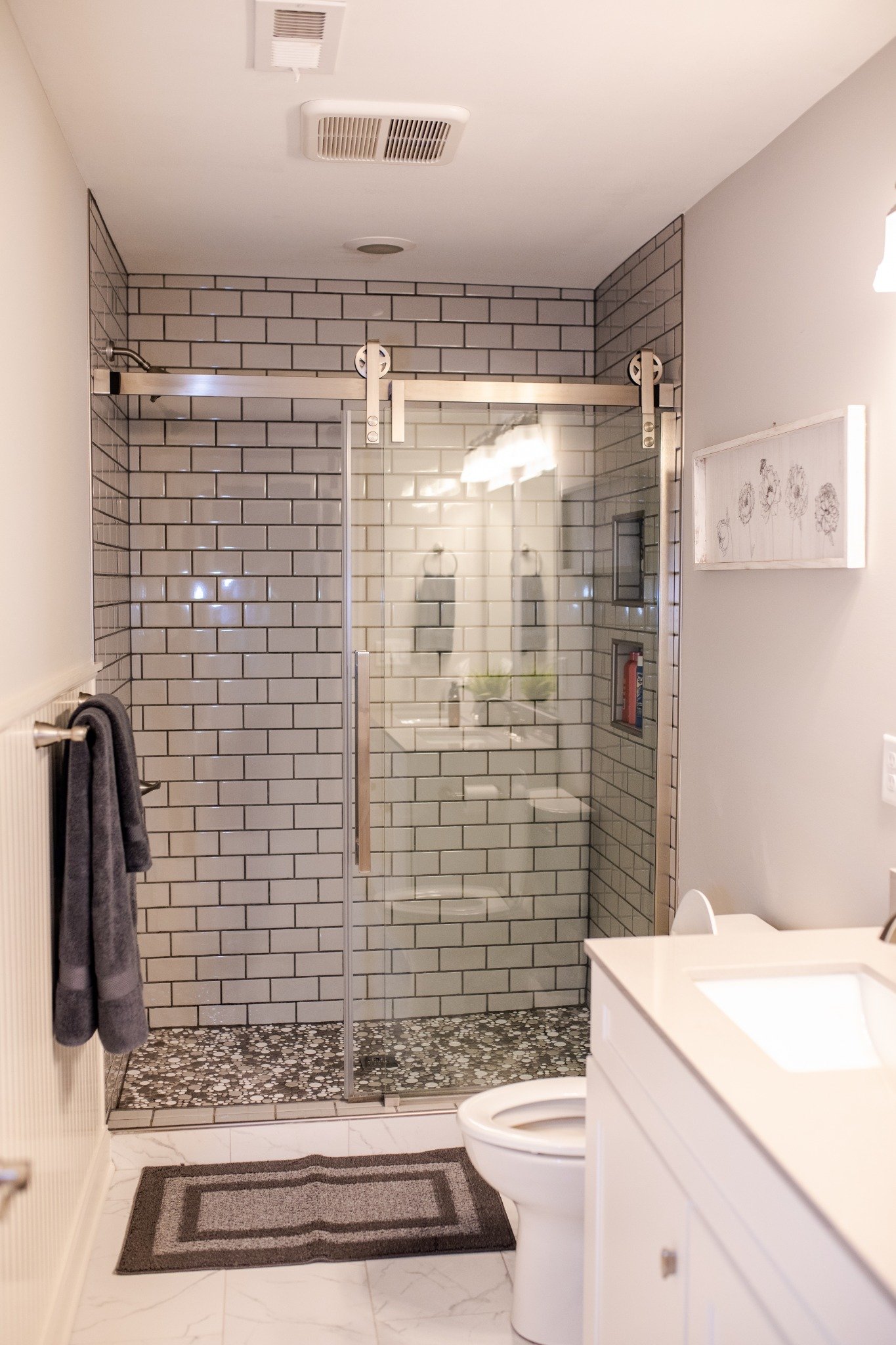 Bathroom at the Manor onsite accommodation at Ramble Creek, featuring a glass walk-in shower with subway tile, pebble tile flooring, white vanity, and neutral finishes.