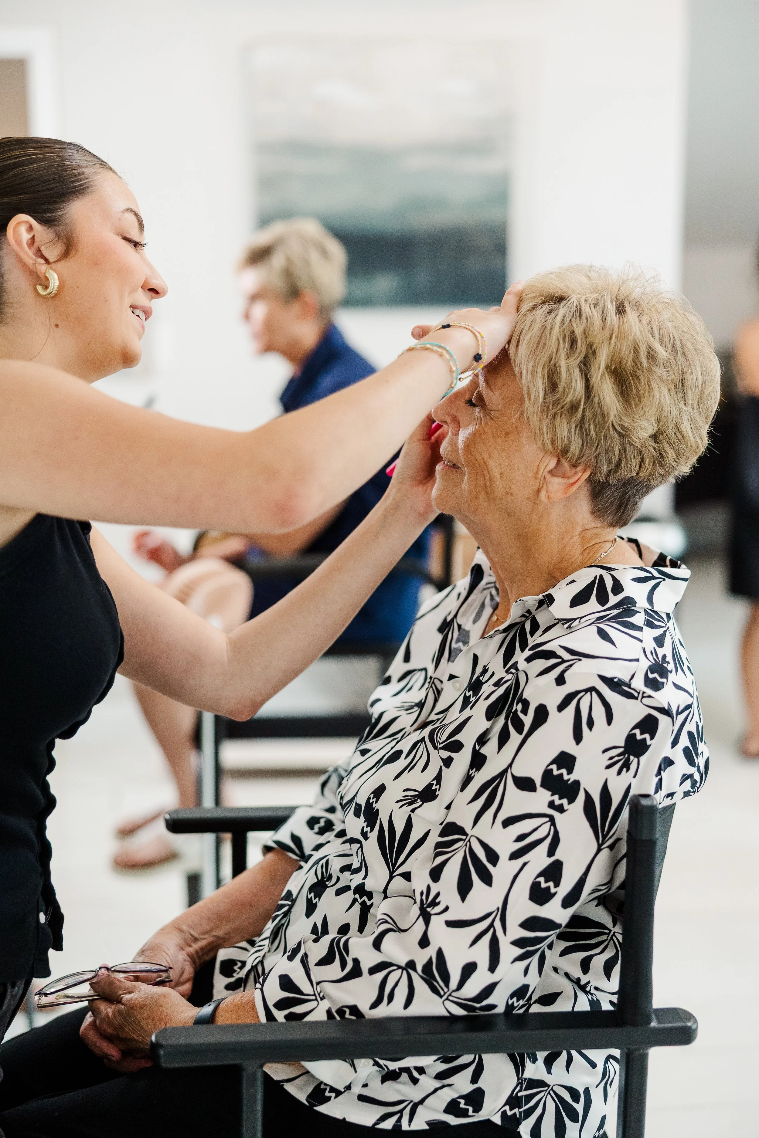 Makeup artist applying finishing touches to an older woman’s wedding guest makeup