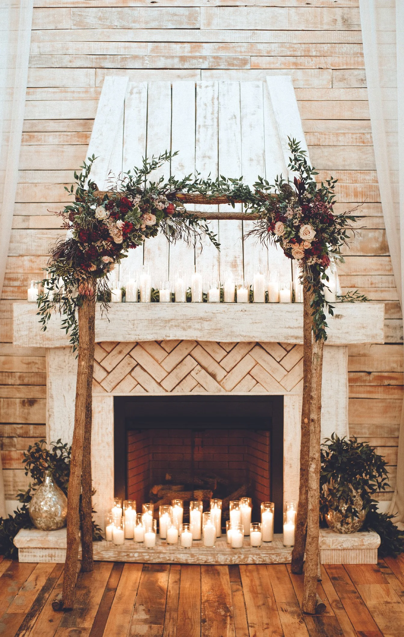 Indoor wedding ceremony arbor at Ramble Creek Wedding Venue in Tennessee with lush floral arrangements, greenery, fireplace decor, and glowing candlelight.