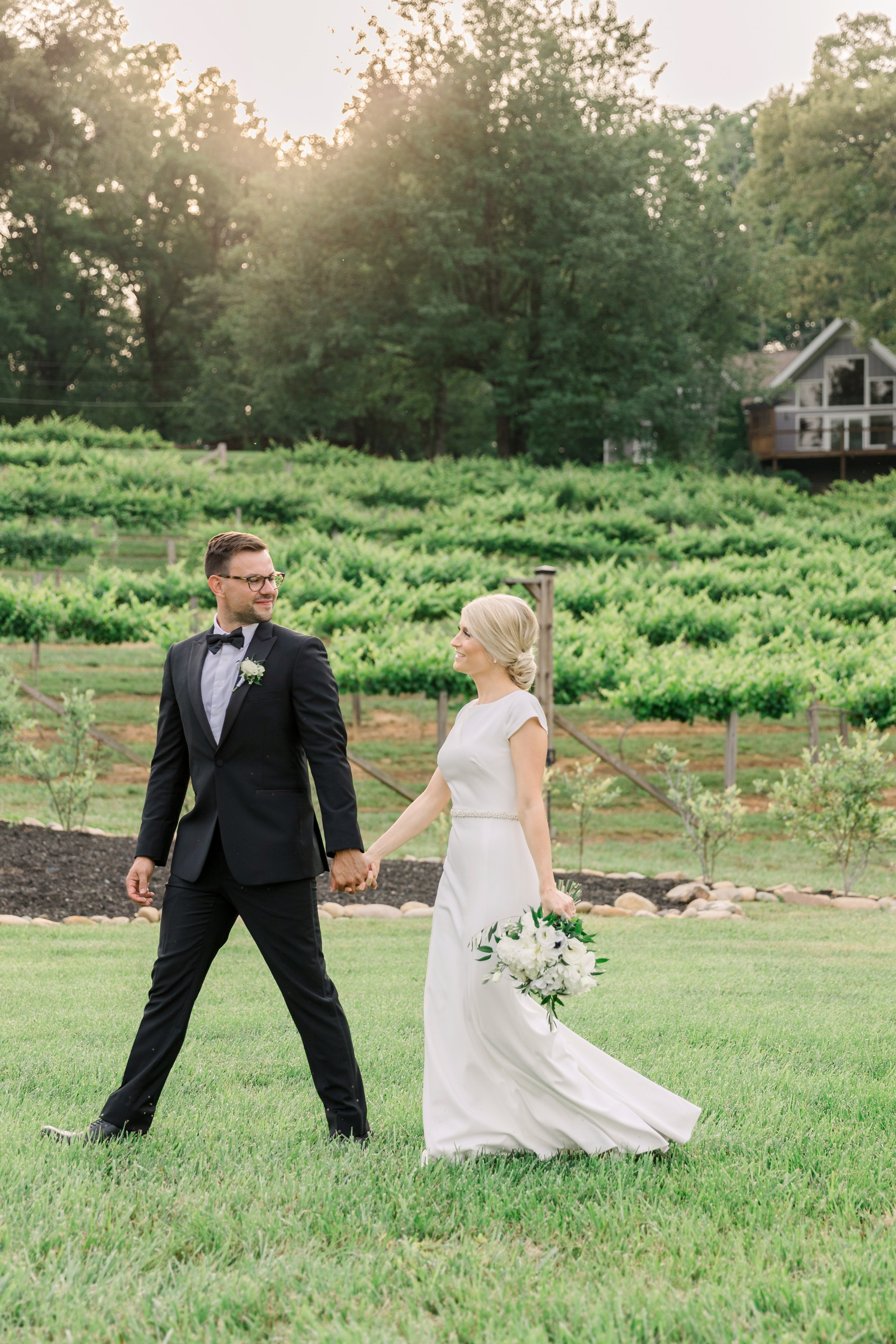 Bride and groom walking hand in hand in front of Ramble Creek’s vineyard during a romantic summer wedding in Tennessee.