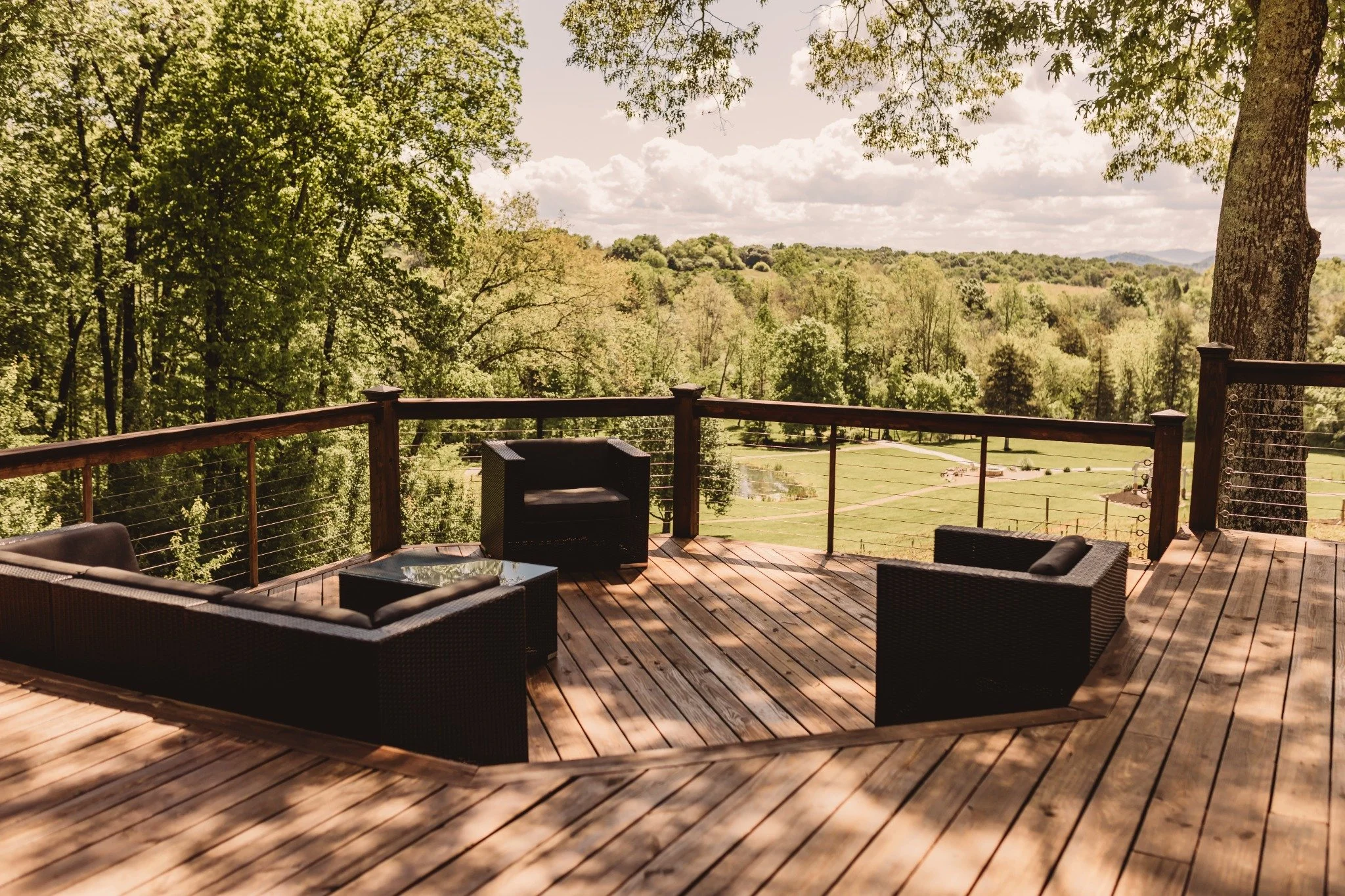 Outdoor deck at the Manor onsite accommodation at Ramble Creek, featuring wicker seating, wood railing, and scenic views of the rolling Tennessee countryside.