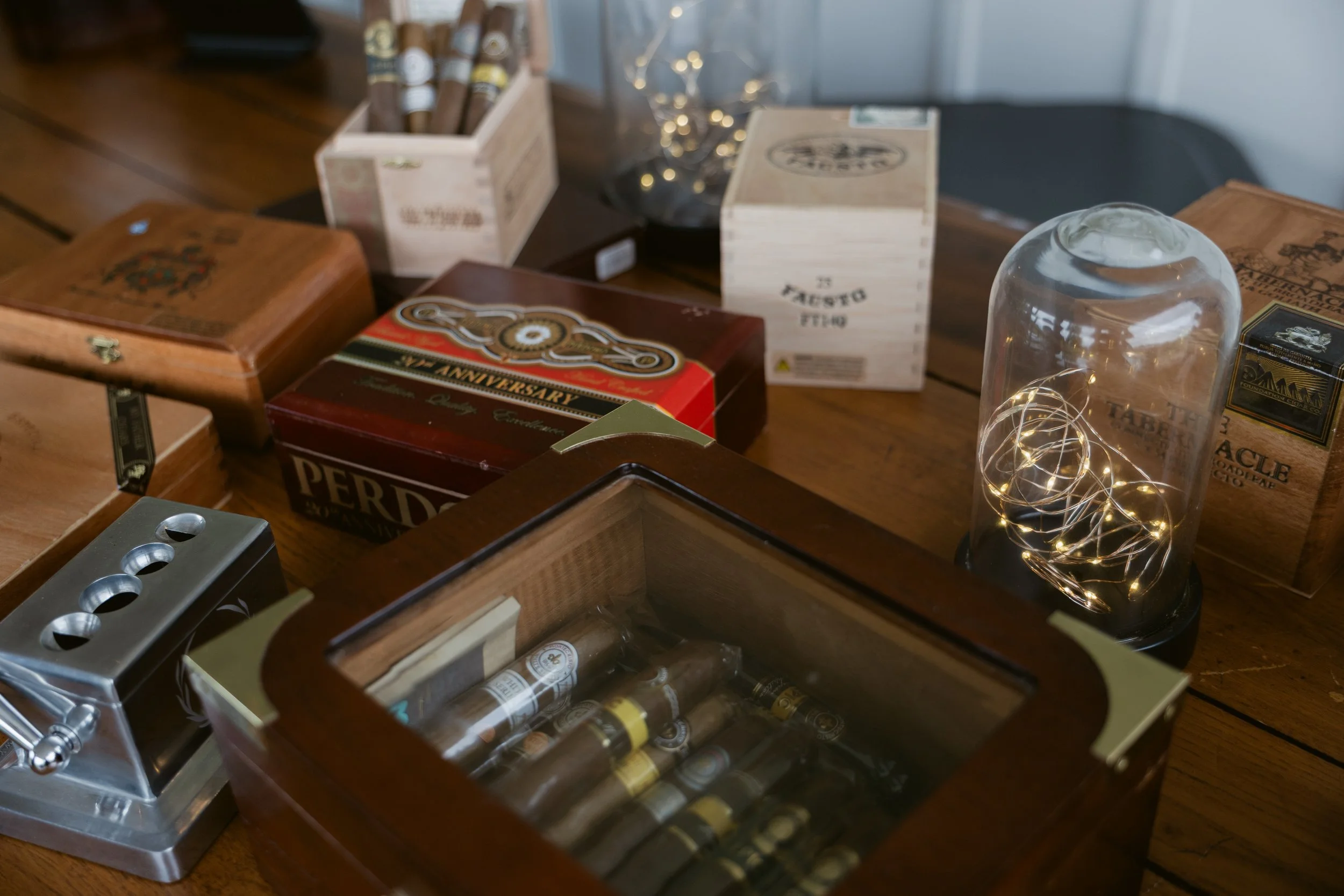 Wedding cigar bar display at Ramble Creek Wedding Venue in Tennessee featuring cigar boxes, a humidor, cutter, and decorative lights.