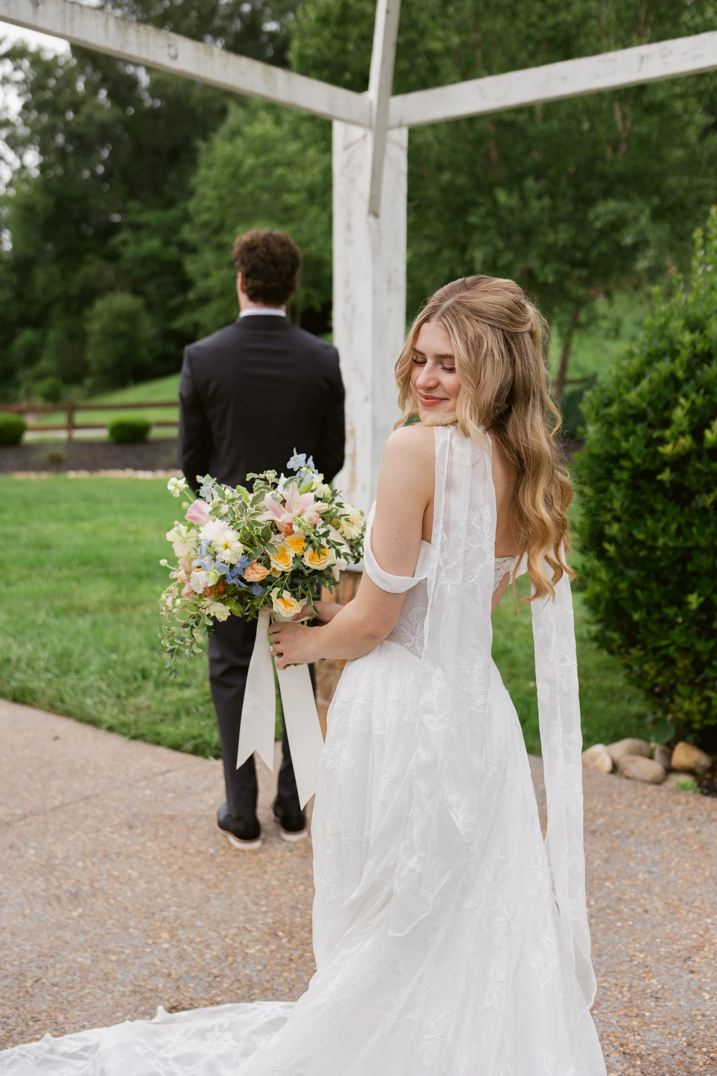 Bride smiling with a pastel floral bouquet before a first look on Ramble Creek’s upper lawn at the Tennessee wedding venue.