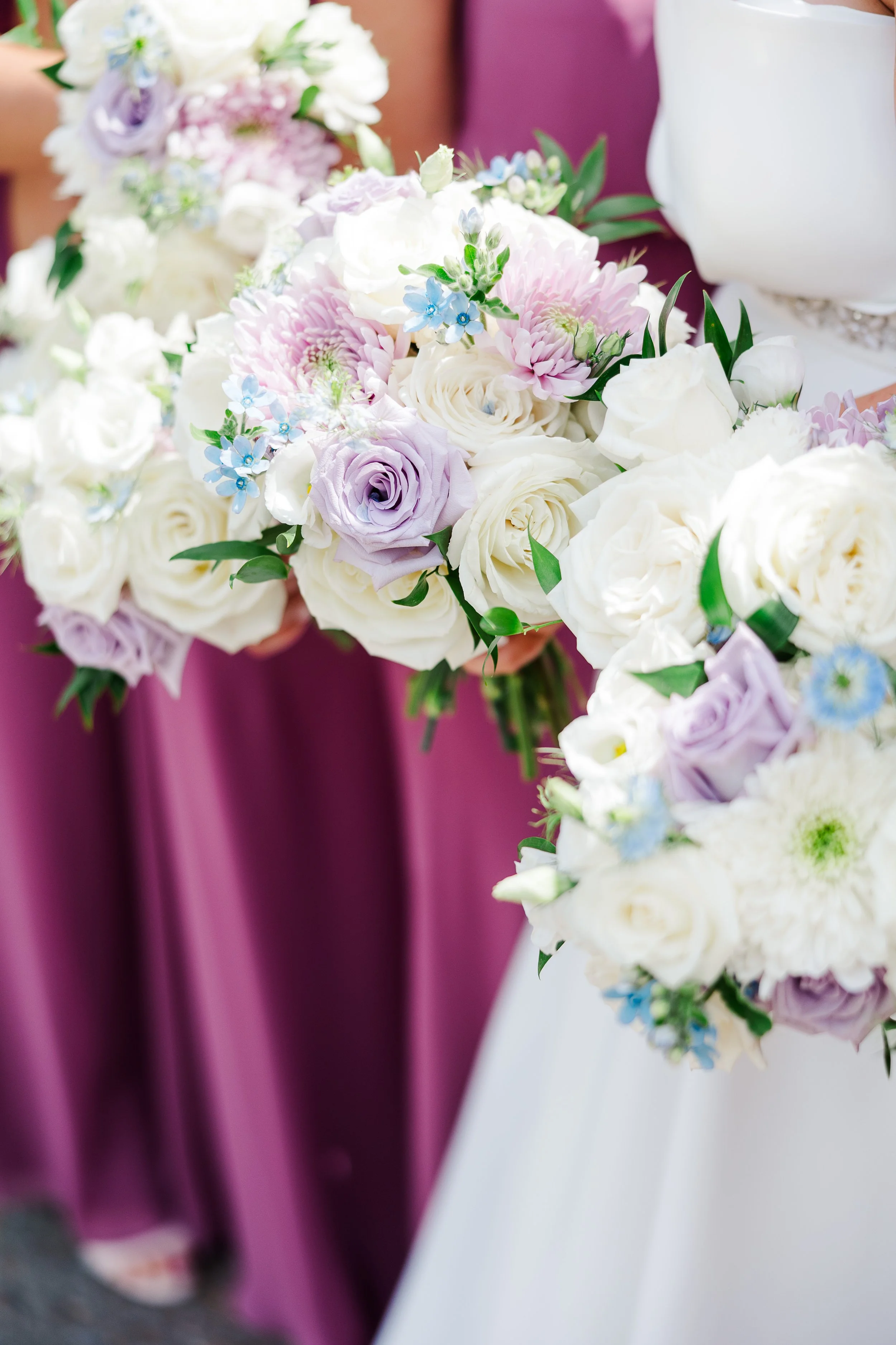 Soft pastel bridesmaids bouquets with white roses, lavender blooms, blush chrysanthemums, and delicate blue accents at Ramble Creek, styled for a romantic spring wedding.