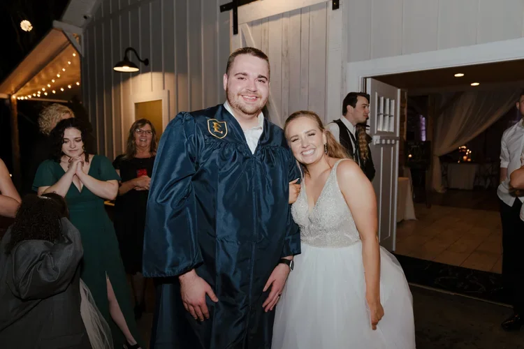Bride posing with a groom in his graduation gown outside the Ramble Creek reception during their Tennessee wedding celebration