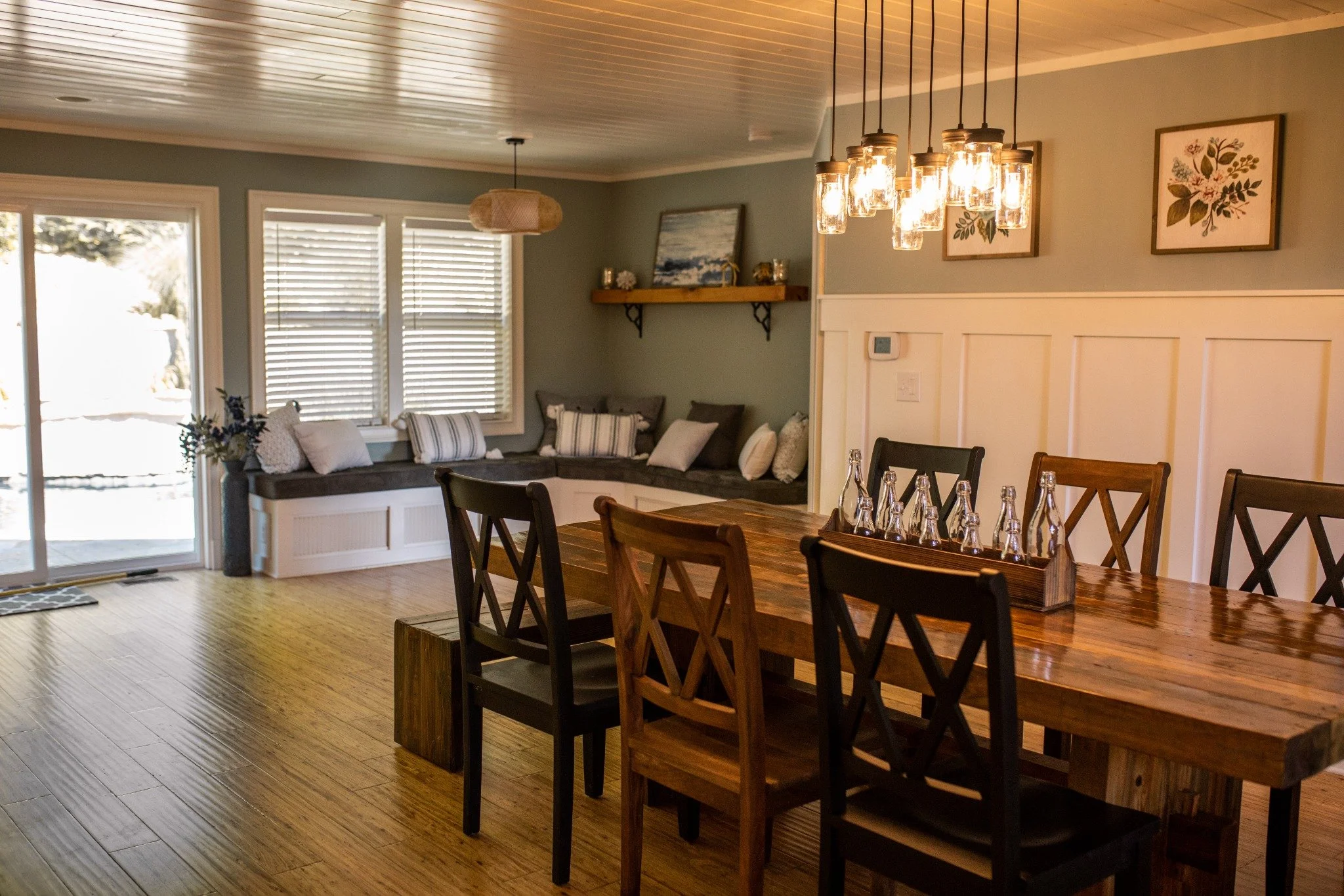 Dining room at the Manor onsite accommodation at Ramble Creek, featuring a long wooden table, warm pendant lighting, built-in window seat lounge, and soft sage green walls.