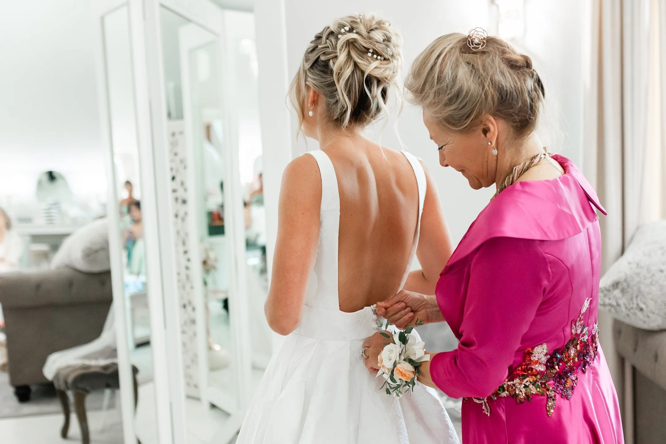 Mother of the bride helps fasten the bride’s white wedding dress in the Ramble Creek bridal suite before the ceremony.