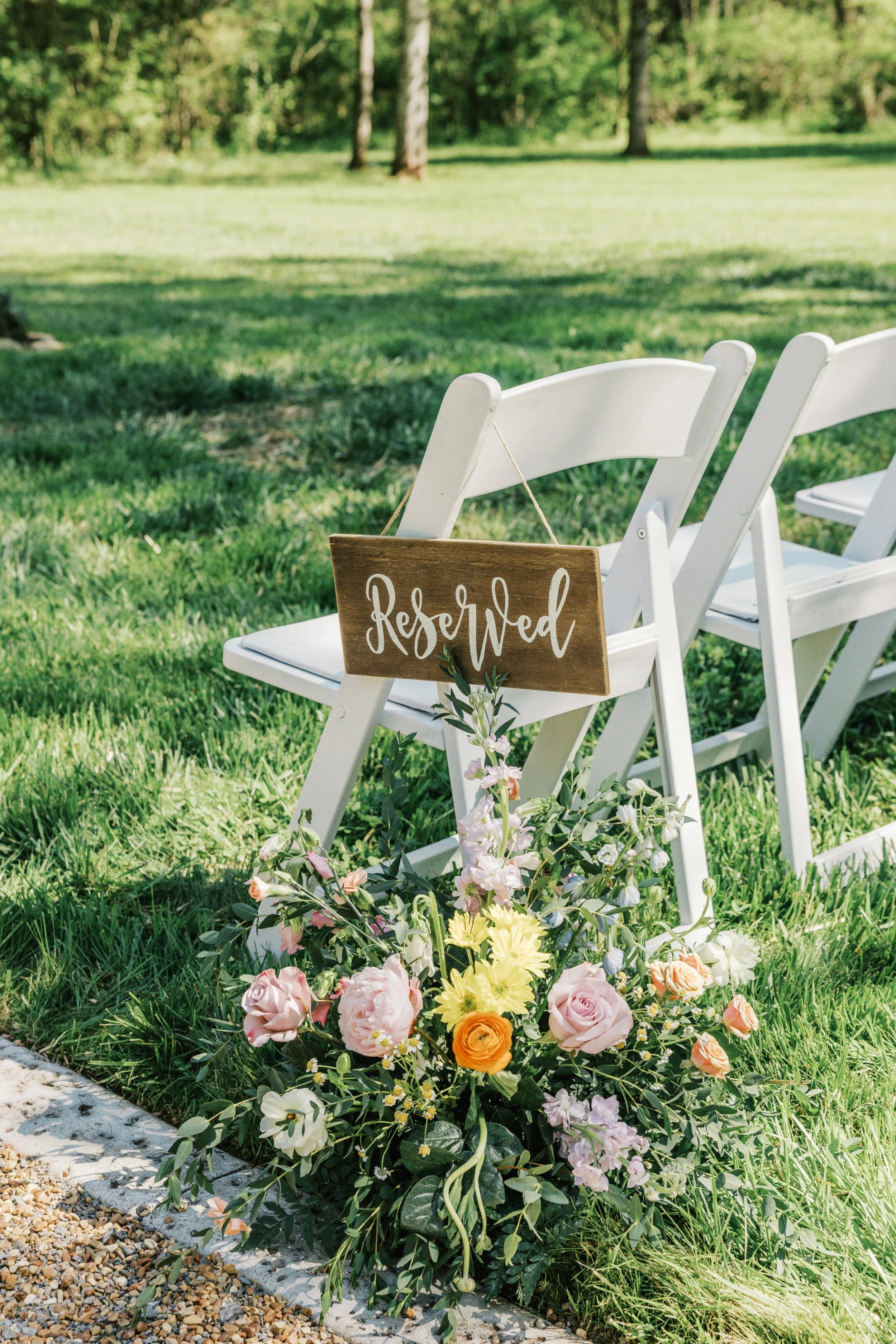 Reserved sign on white ceremony chairs at Ramble Creek with pastel floral arrangements marking family seating in the outdoor wedding ceremony space.