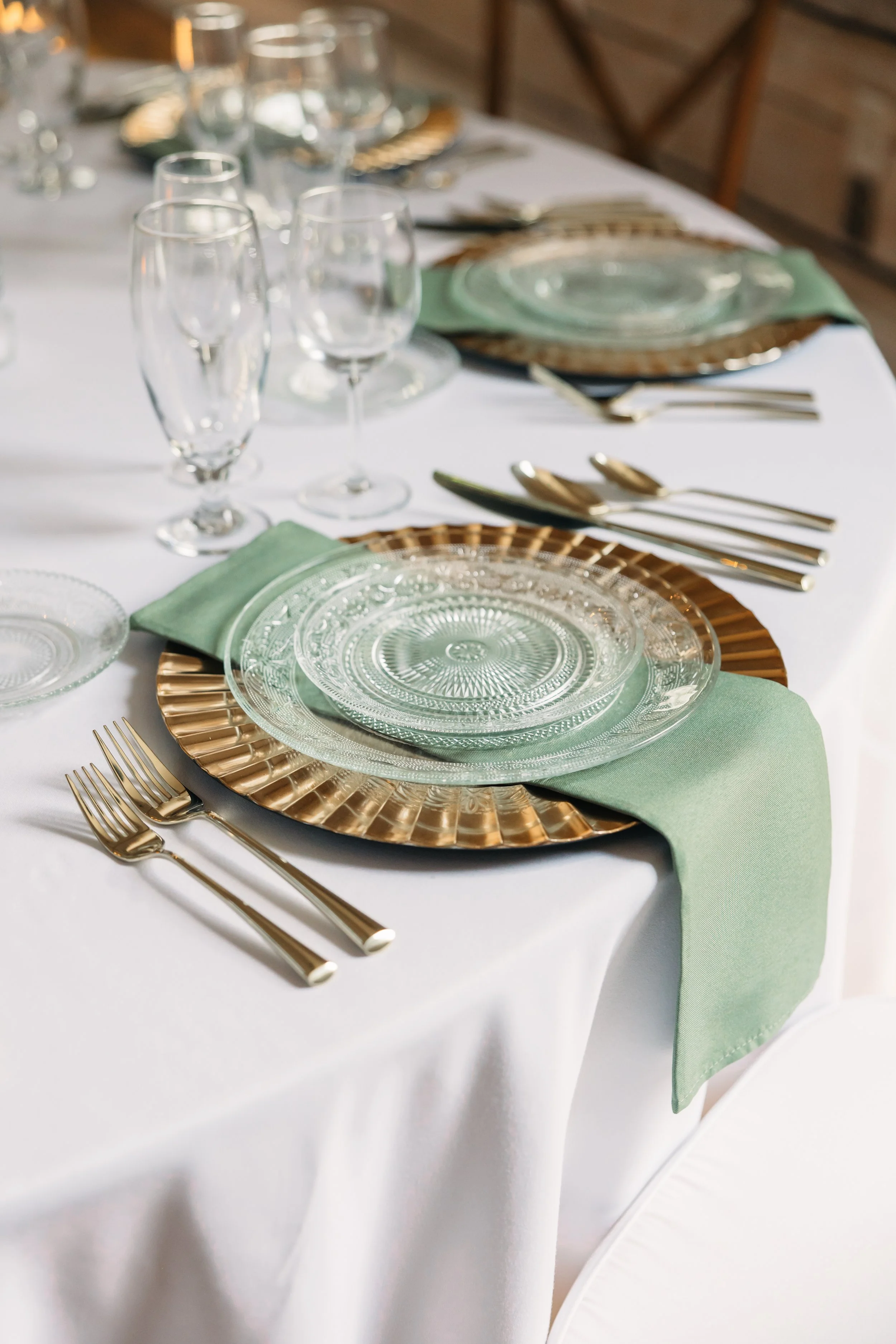 Wedding reception place setting at Ramble Creek with sage napkin, gold charger, glass plates, gold flatware, and elegant glassware