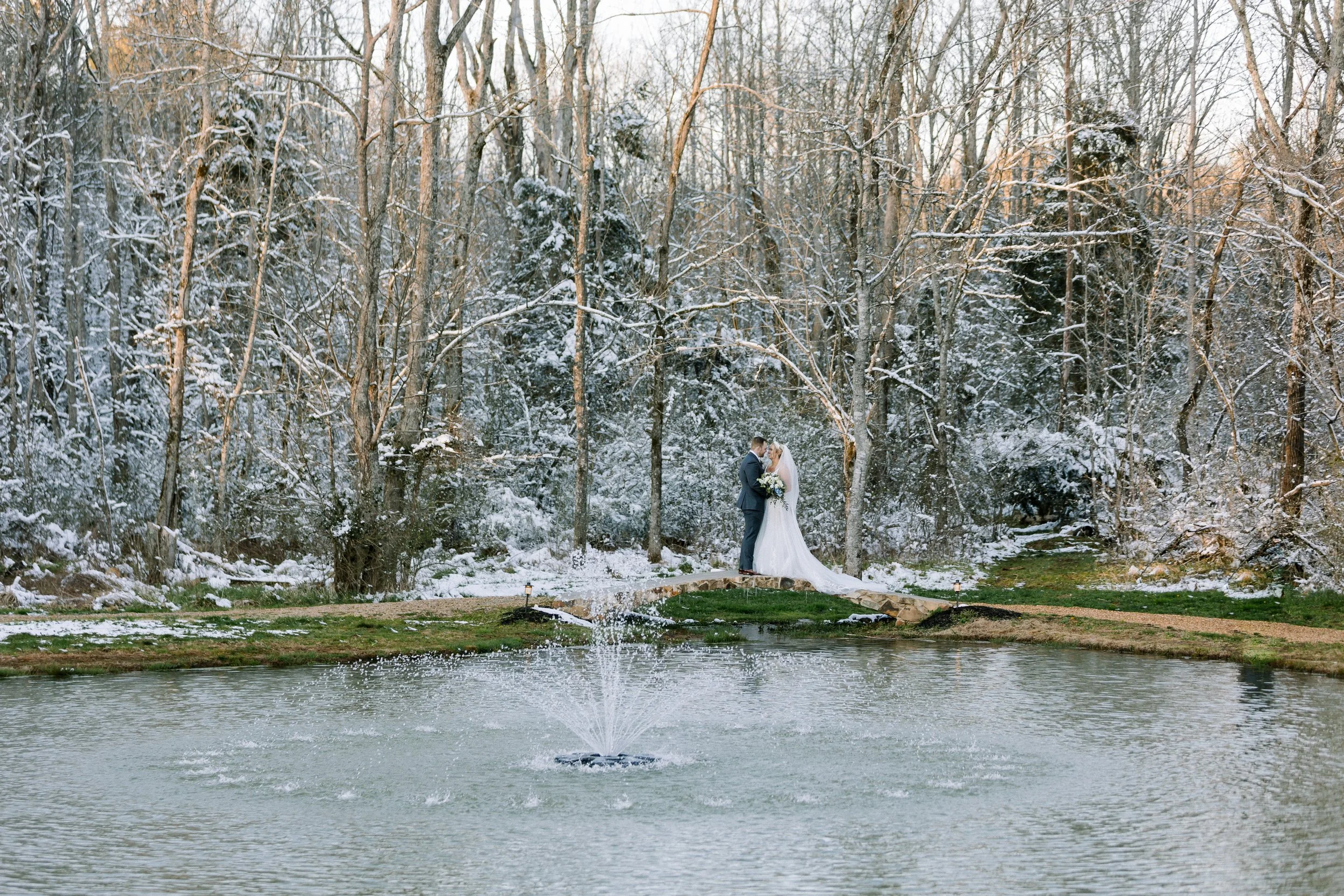 Bride and groom sharing a winter wedding portrait by the pond at Ramble Creek, surrounded by snow-covered trees in Tennessee