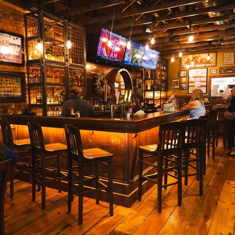 Wooden bar at The Lazy Beagle in Sweetwater, TN, with tall stools, illuminated liquor shelves, exposed brick, and hanging lights