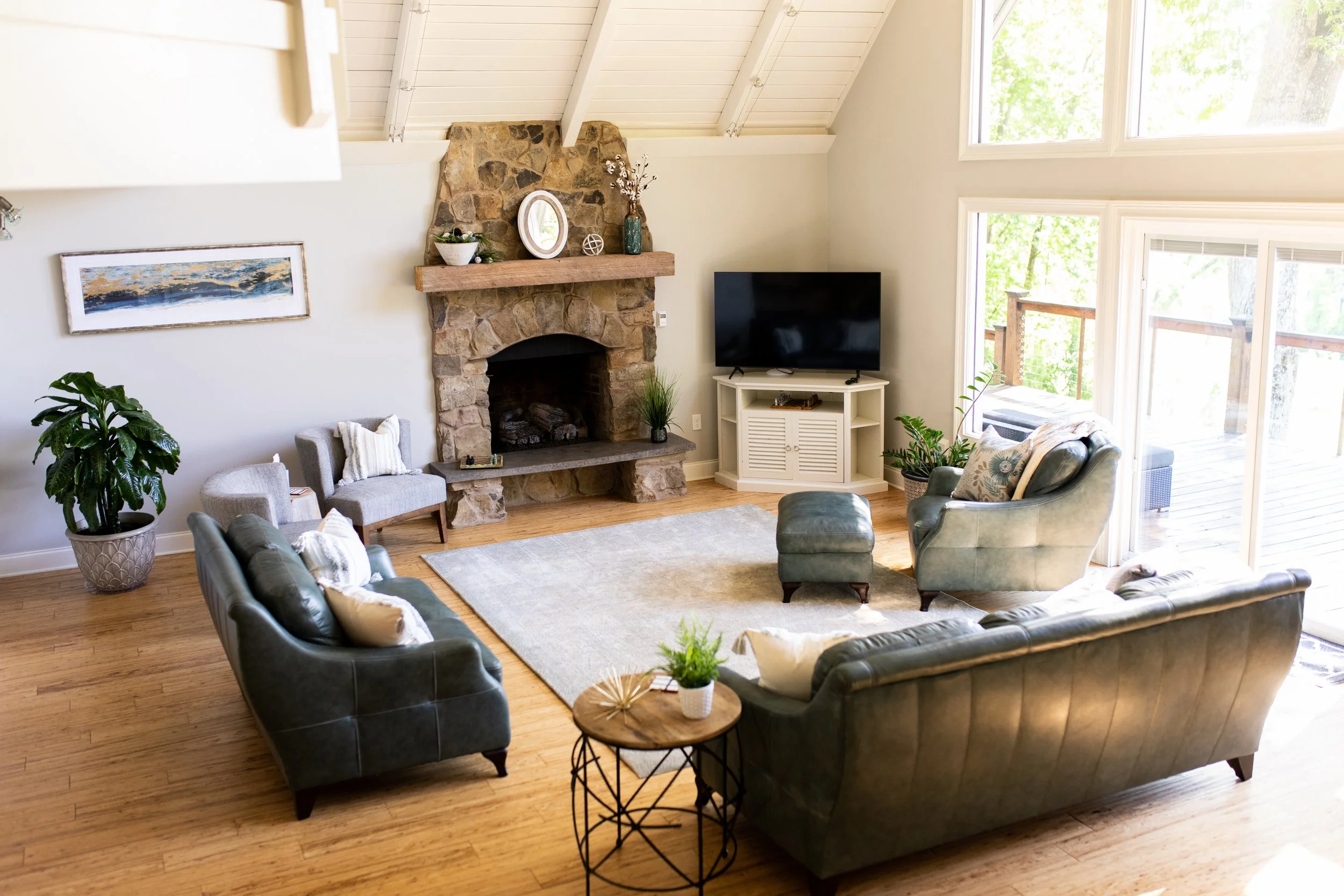 Bright living room at the Manor onsite accommodation at Ramble Creek, featuring leather seating, a stone fireplace, TV, large windows, and access to an outdoor deck.