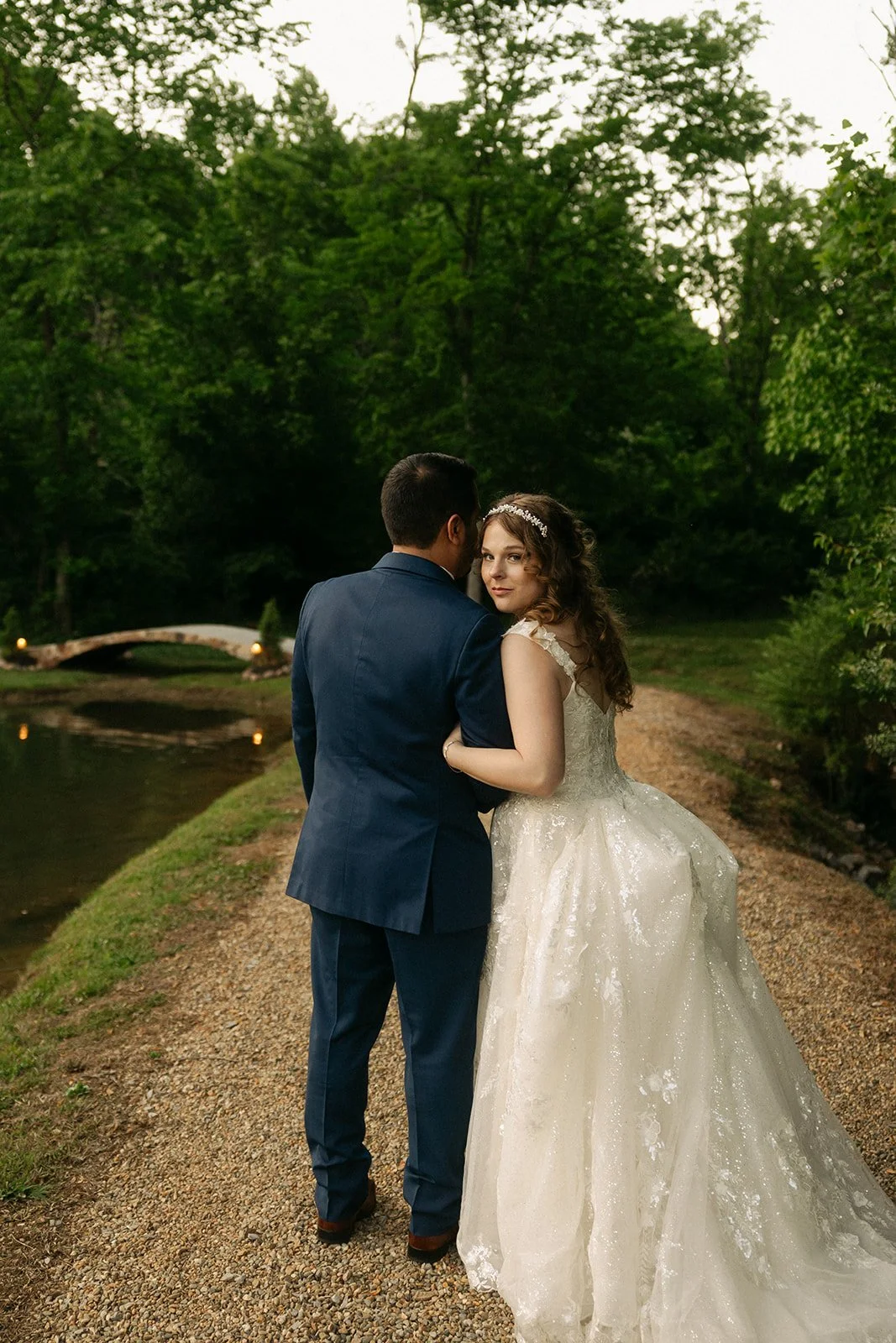 Bride and groom walking beside the pond at Ramble Creek, a romantic Tennessee wedding venue with wooded scenery, soft pathway lighting, and lush outdoor portrait locations