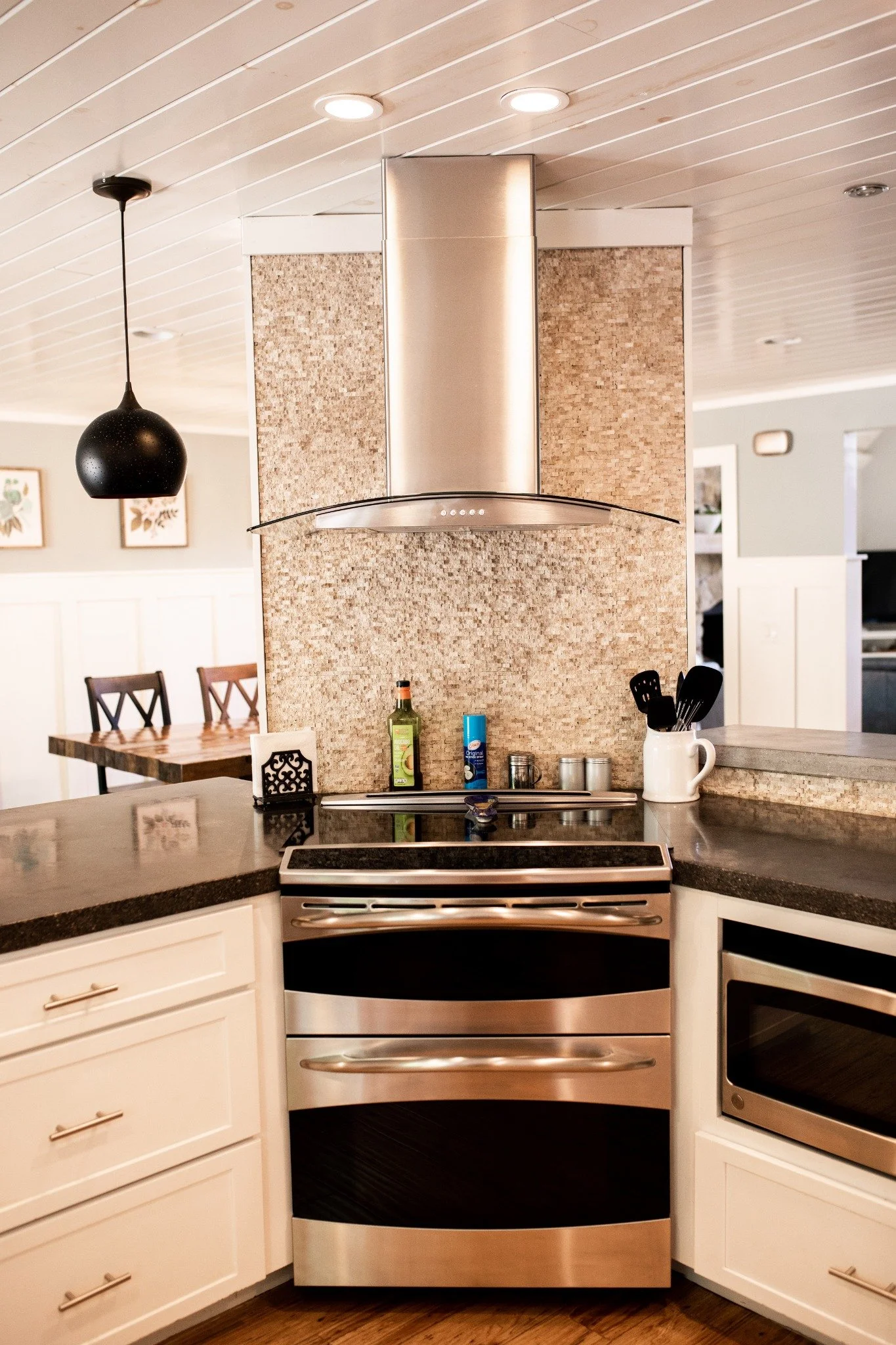 Kitchen at the Manor onsite accommodation at Ramble Creek, featuring a stainless steel range, modern range hood, tile backsplash, white cabinetry, and dark countertops.
