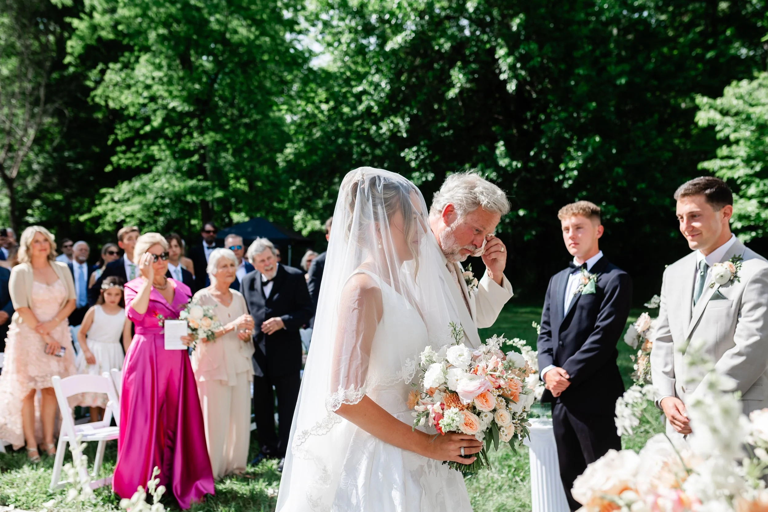 Bride walks down the outdoor ceremony aisle with her father at Ramble Creek as guests and the groom look on.