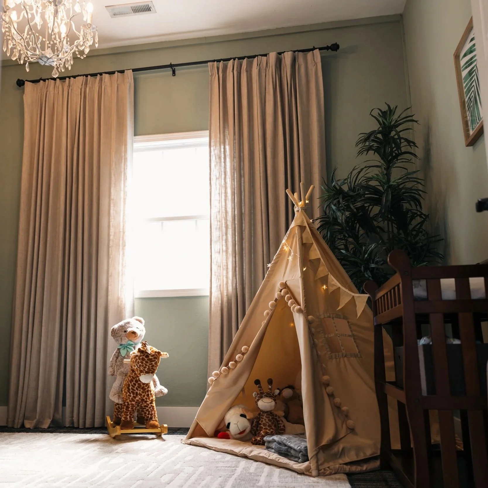 Kids' play room at family-friendly wedding venue. Room has beige curtains, a teddy bear on a rocking horse, a toy giraffe, plush giraffe, zebra, and lion inside a beige play tent, next to a tall green plant and framed wall art.