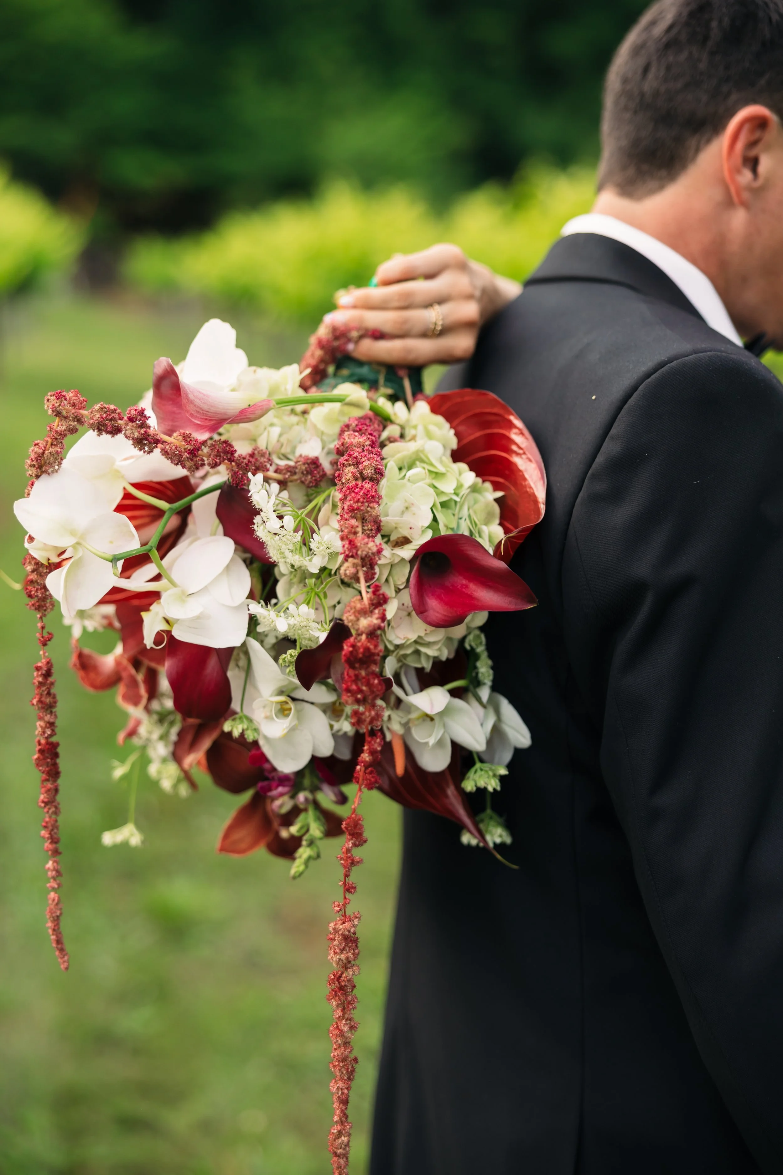 Dramatic bridal bouquet with burgundy calla lilies, white orchids, hydrangeas, and cascading florals carried during an outdoor wedding at Ramble Creek.