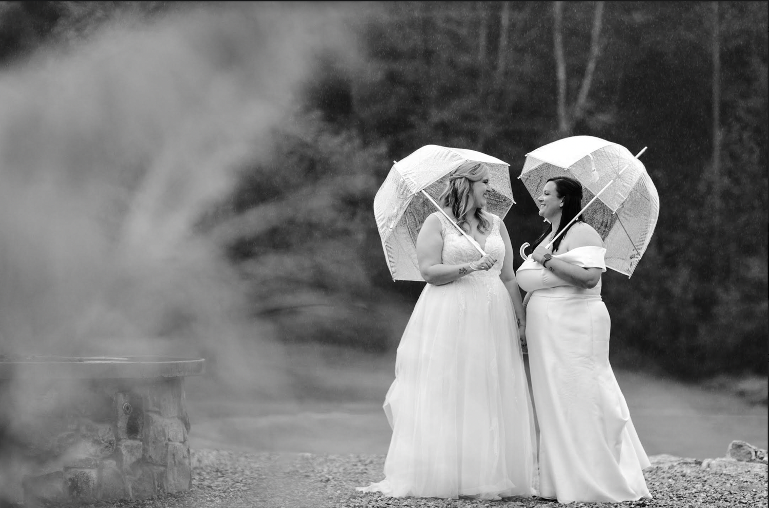 Two brides on their wedding day at Ramble Creek, holding umbrellas, black and white filter