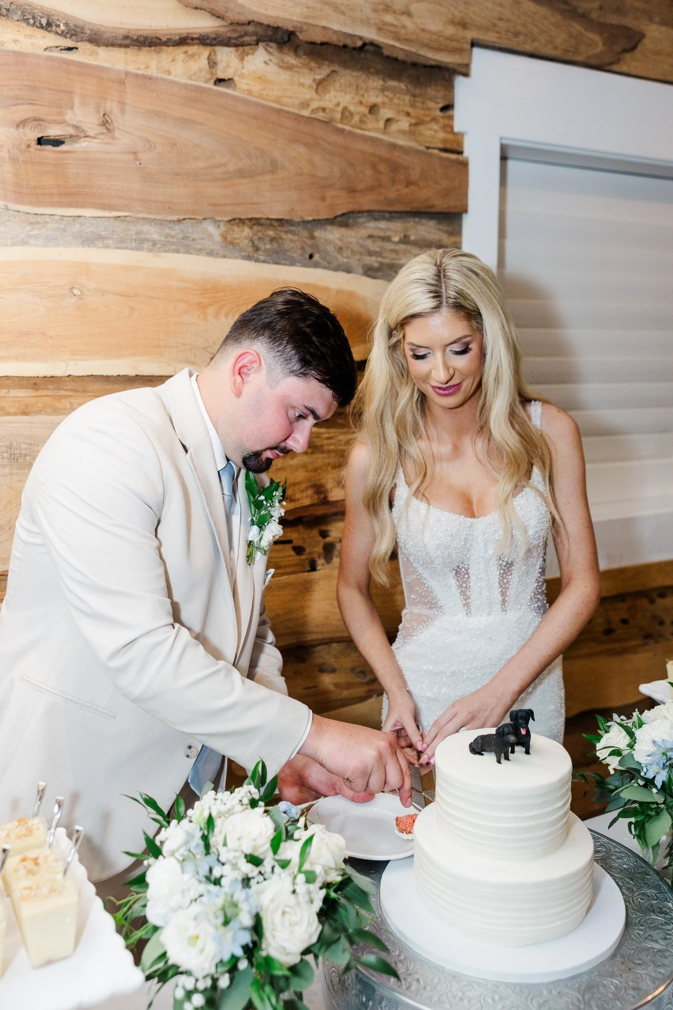 Couple cutting a white wedding cake with dog cake toppers during their Ramble Creek reception.