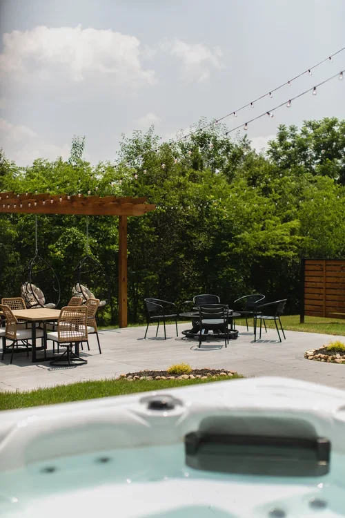 View from the hot tub at the Villa at Ramble Creek, overlooking the backyard patio with fire pit seating, outdoor dining, hanging chairs, and string lights.