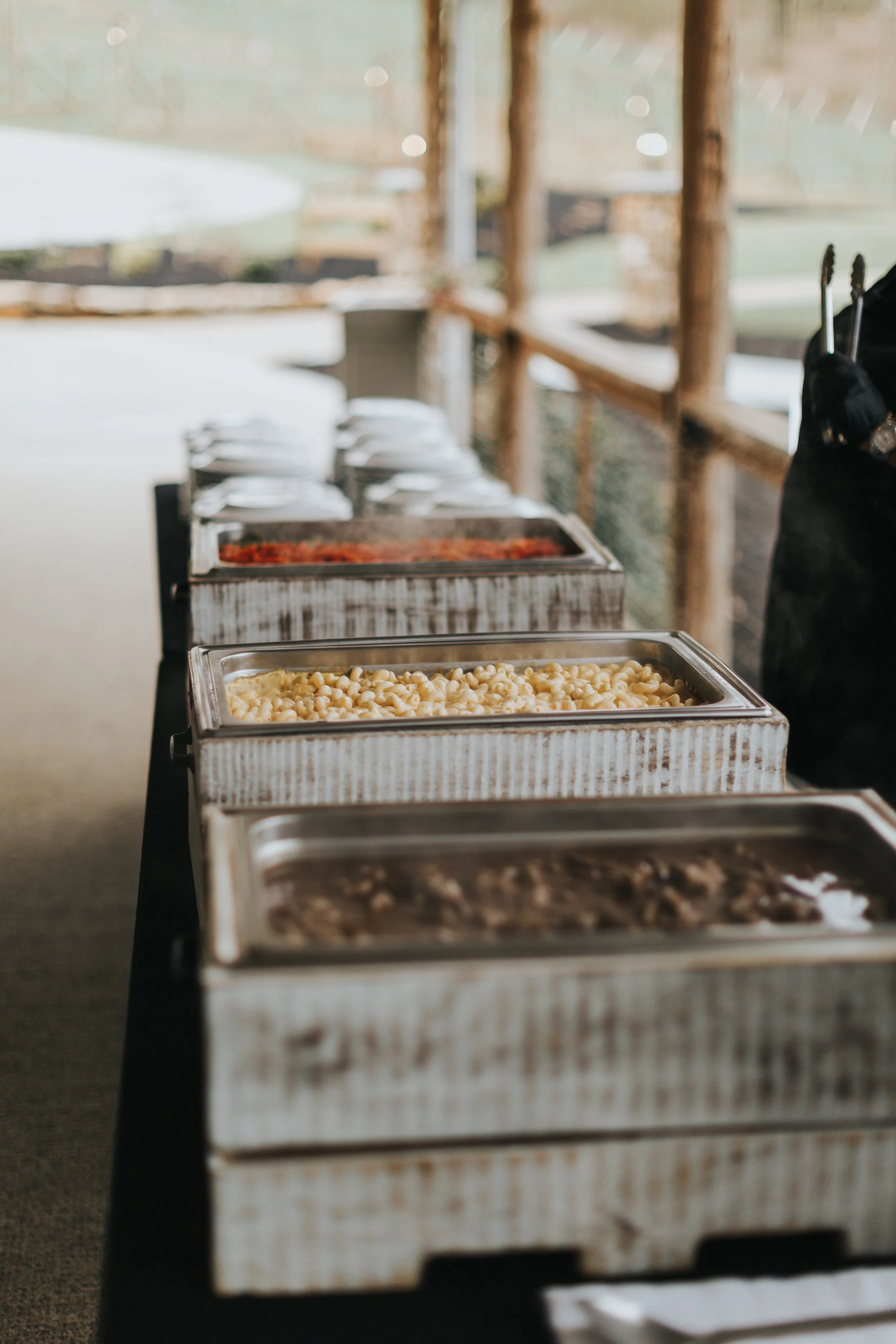 Exceptional wedding buffet table with several trays of food, including macaroni and cheese, chili, and other dishes, set outdoors in covered area.