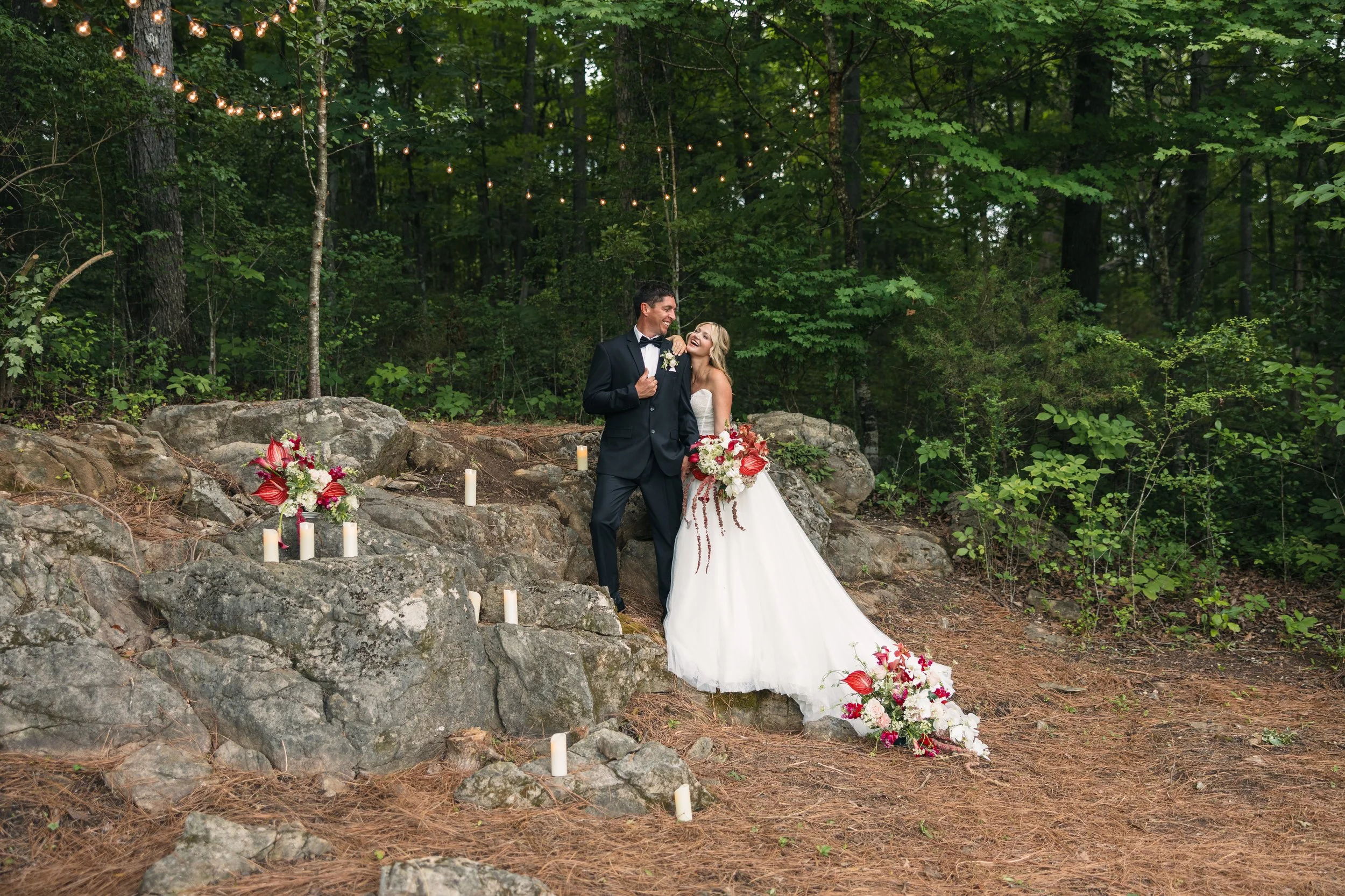 Bride and groom posing among woodland rocks, candlelight, string lights, and bold floral arrangements at Ramble Creek Wedding Venue in Tennessee