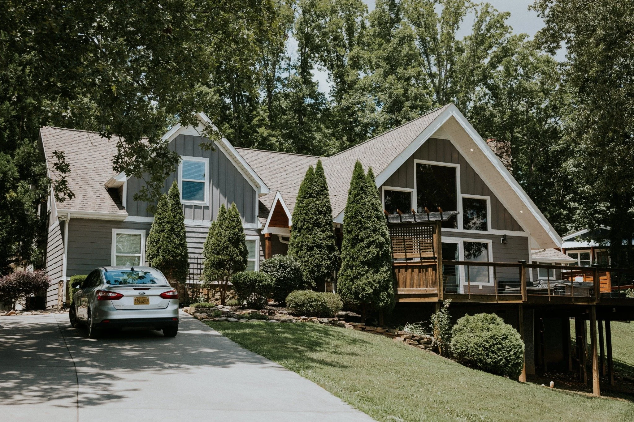 Exterior of the Manor onsite accommodation at Ramble Creek, featuring gray siding, large windows, landscaped greenery, a driveway, and spacious wooden deck.
