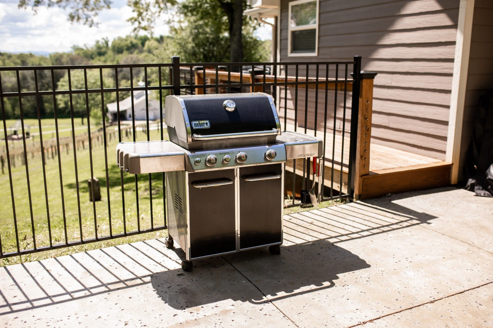Outdoor grill patio at the Manor onsite accommodation at Ramble Creek, featuring a stainless steel grill, fenced patio area, and scenic countryside views.