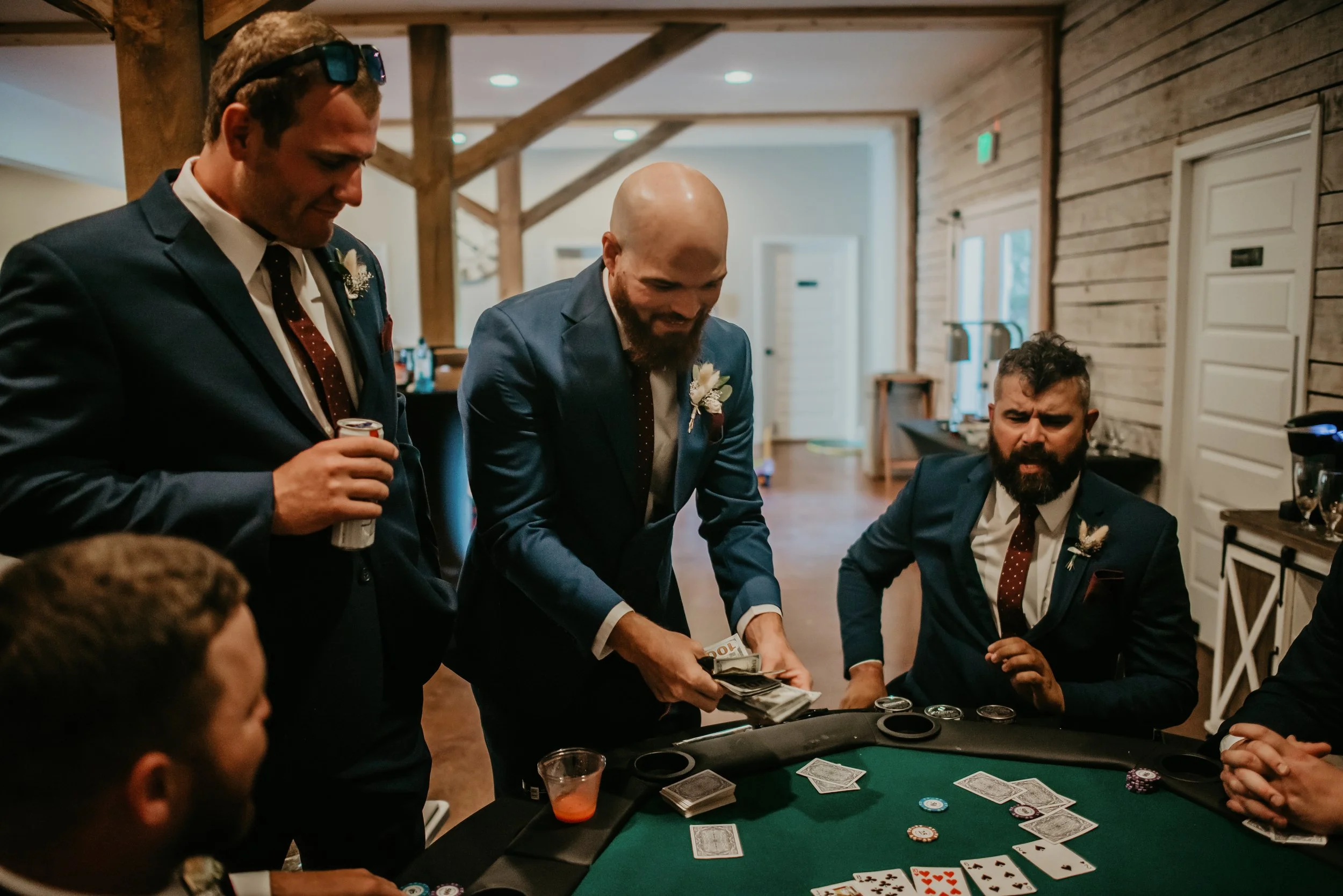 Men in suits playing poker in the Ramble Creek private groom's quarters. One man is holding chips, and there are cards and poker chips on the table.