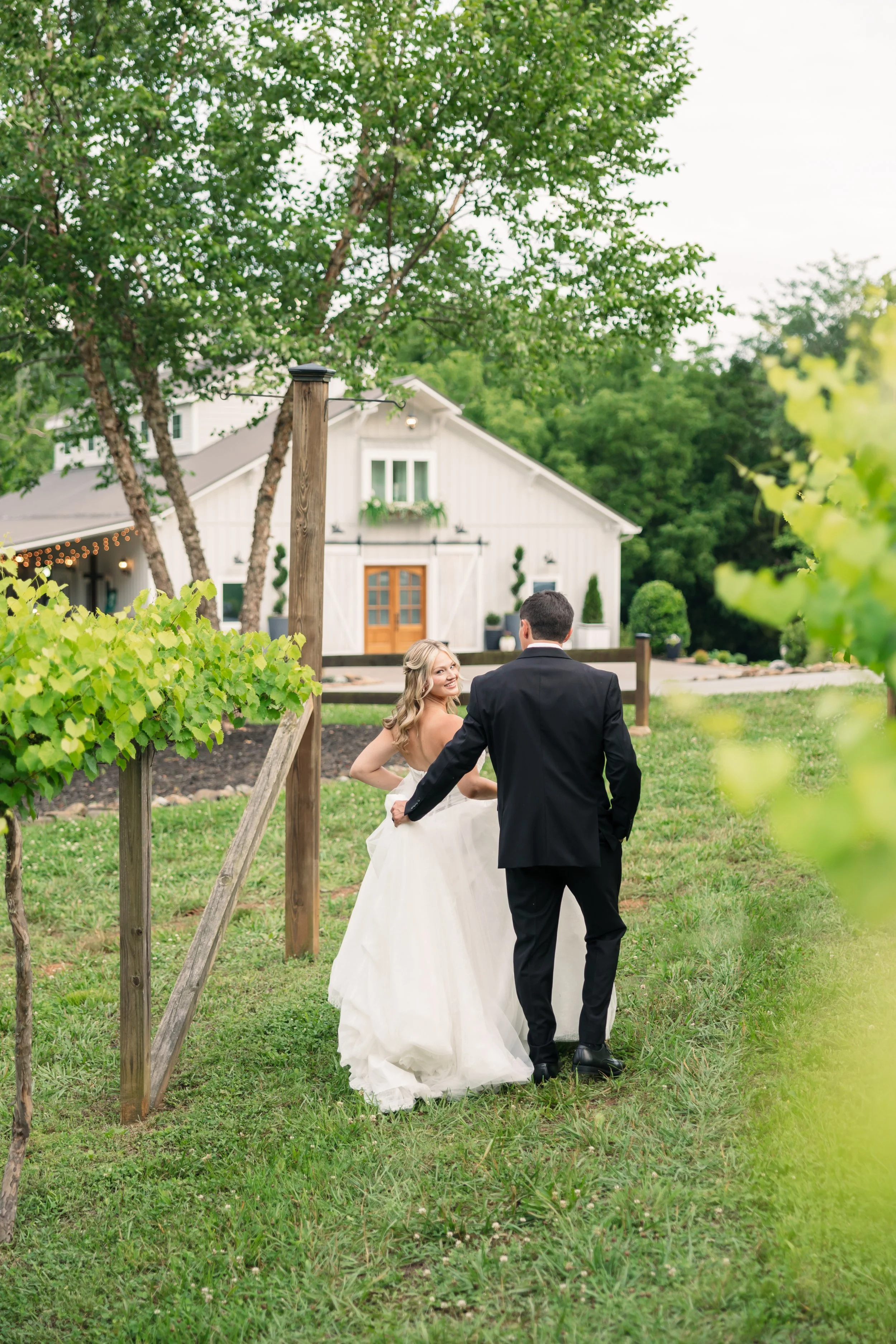 Bride and groom walking through the vineyard at Ramble Creek Wedding Venue with the white venue exterior in the background
