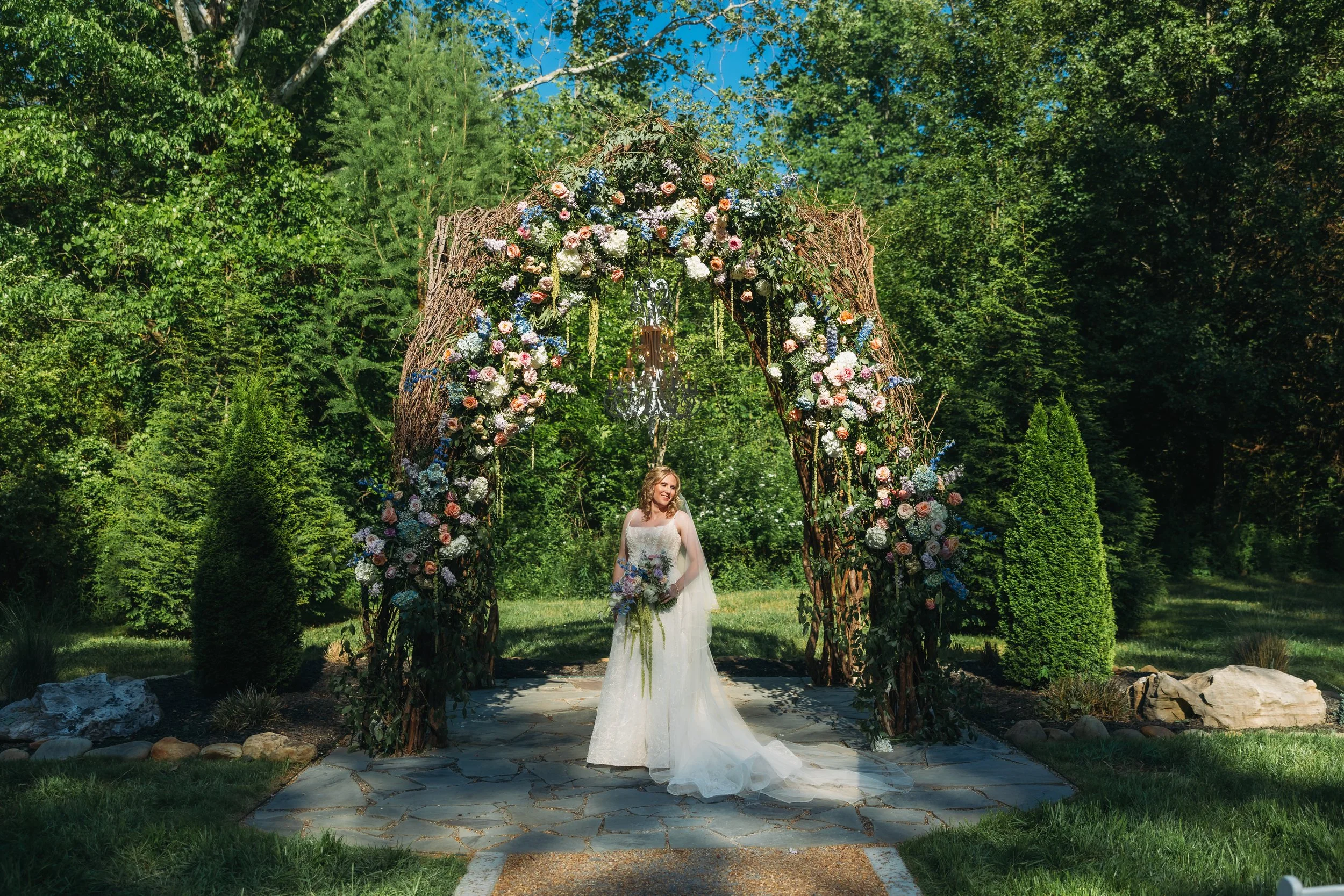 Bride standing beneath Ramble Creek’s vine arbor filled with colorful spring florals for a romantic outdoor wedding ceremony in Tennessee.