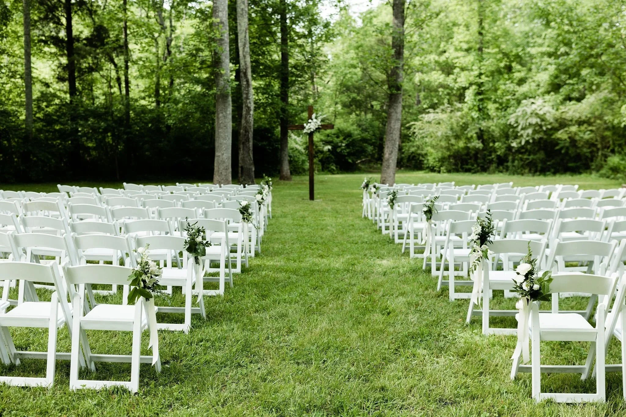 The Lower Lawn outdoor wedding ceremony site at Ramble Creek with white ceremony chairs, greenery aisle decor, and a natural wooded backdrop in East Tennessee.