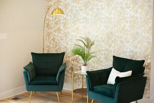 Cozy seating area inside the Villa at Ramble Creek, featuring two green accent chairs, a gold floor lamp, potted plant, and soft patterned wallpaper.