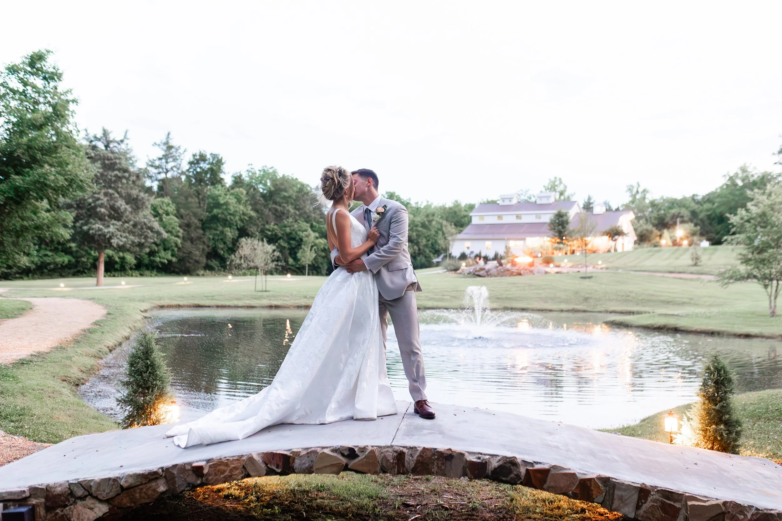 Newlyweds kissing on the stone bridge at Ramble Creek, a  destination Tennessee wedding venue with a pond, fountain, indoor reception area, and scenic outdoor portrait locations
