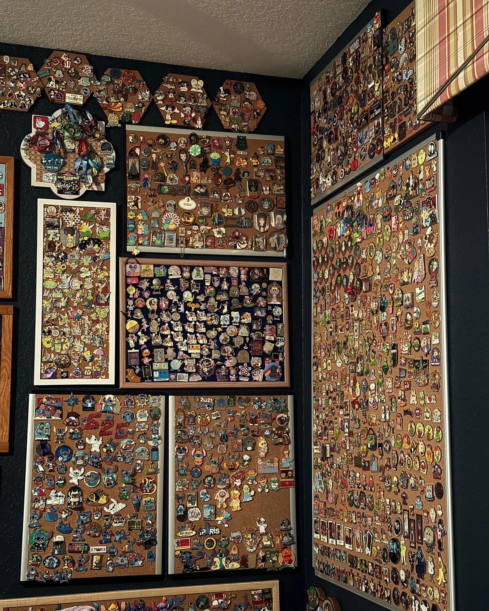Wall display of numerous pins and badges arranged on panels and boards, featuring characters, logos, and designs from various pop culture, movies, and cartoons.