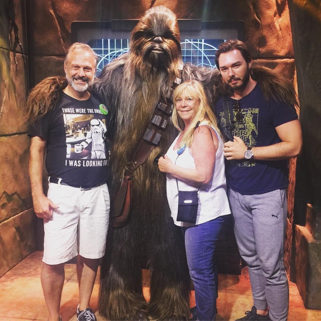 Four people, three men and one woman, posing with a life-sized Chewbacca figure from Star Wars in a themed setting.