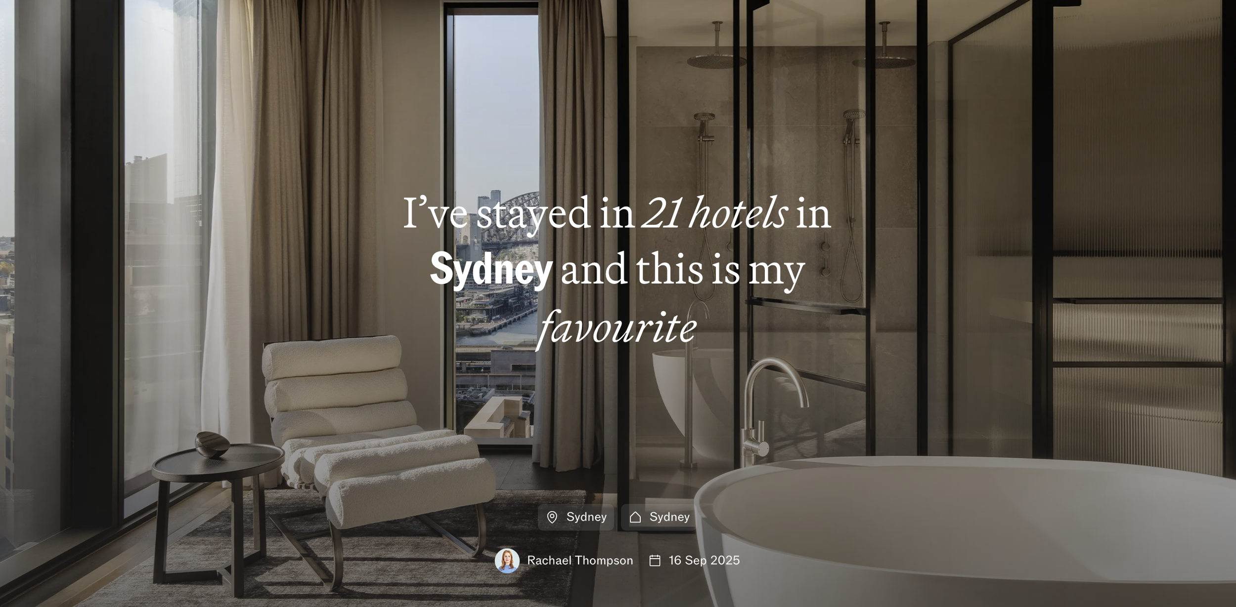 Modern hotel room with a sitting area, large windows, and a bathroom with glass shower doors.