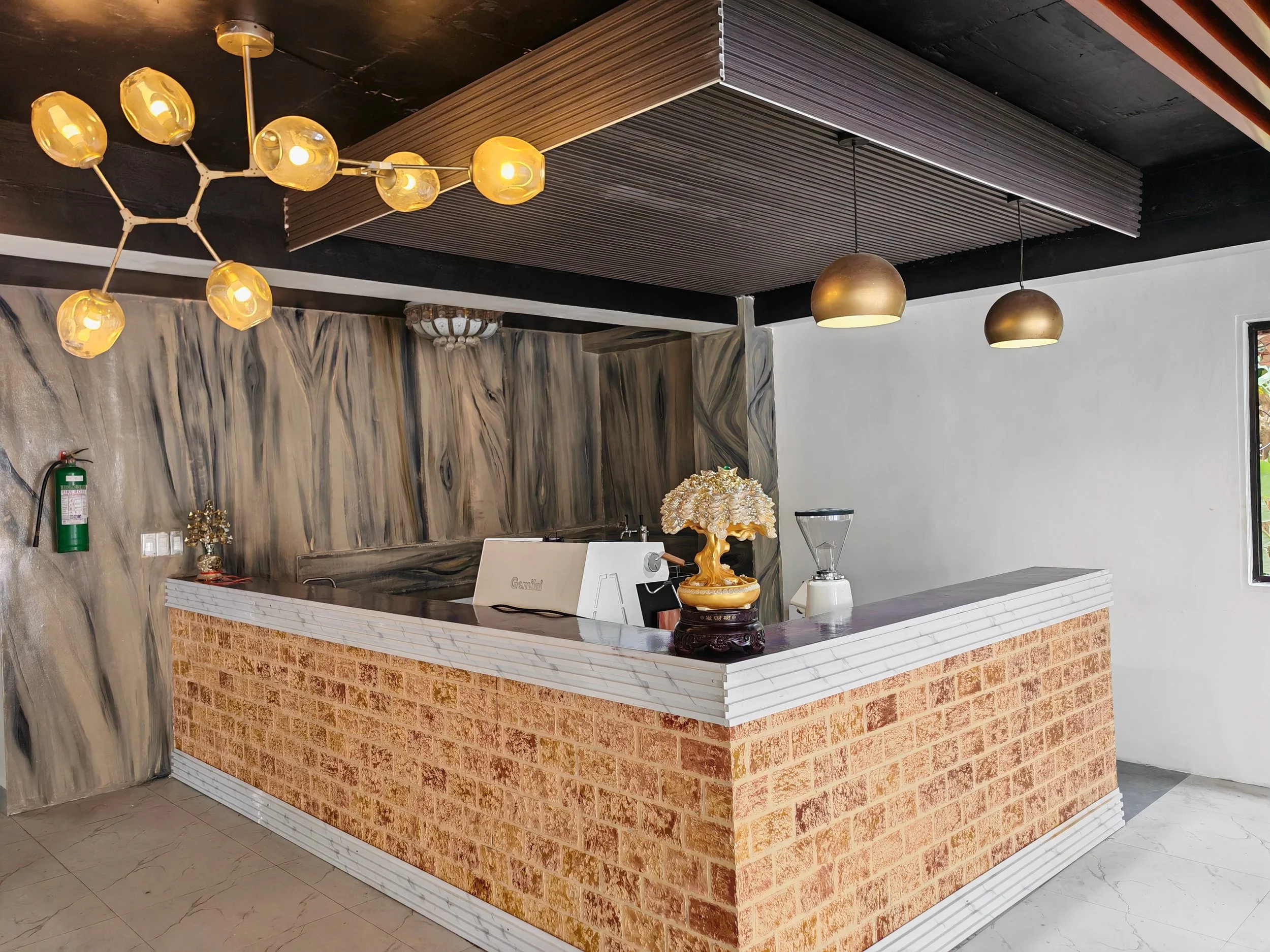Indoor space featuring a exposed brick counter, decorative items, and hanging pendant lights with two additional ceiling lights, set against a gray and black ceiling with one section covered in wood slats.
