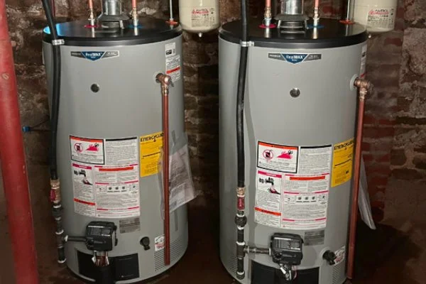 Two Rheem water heaters installed in a basement with a brick wall background.