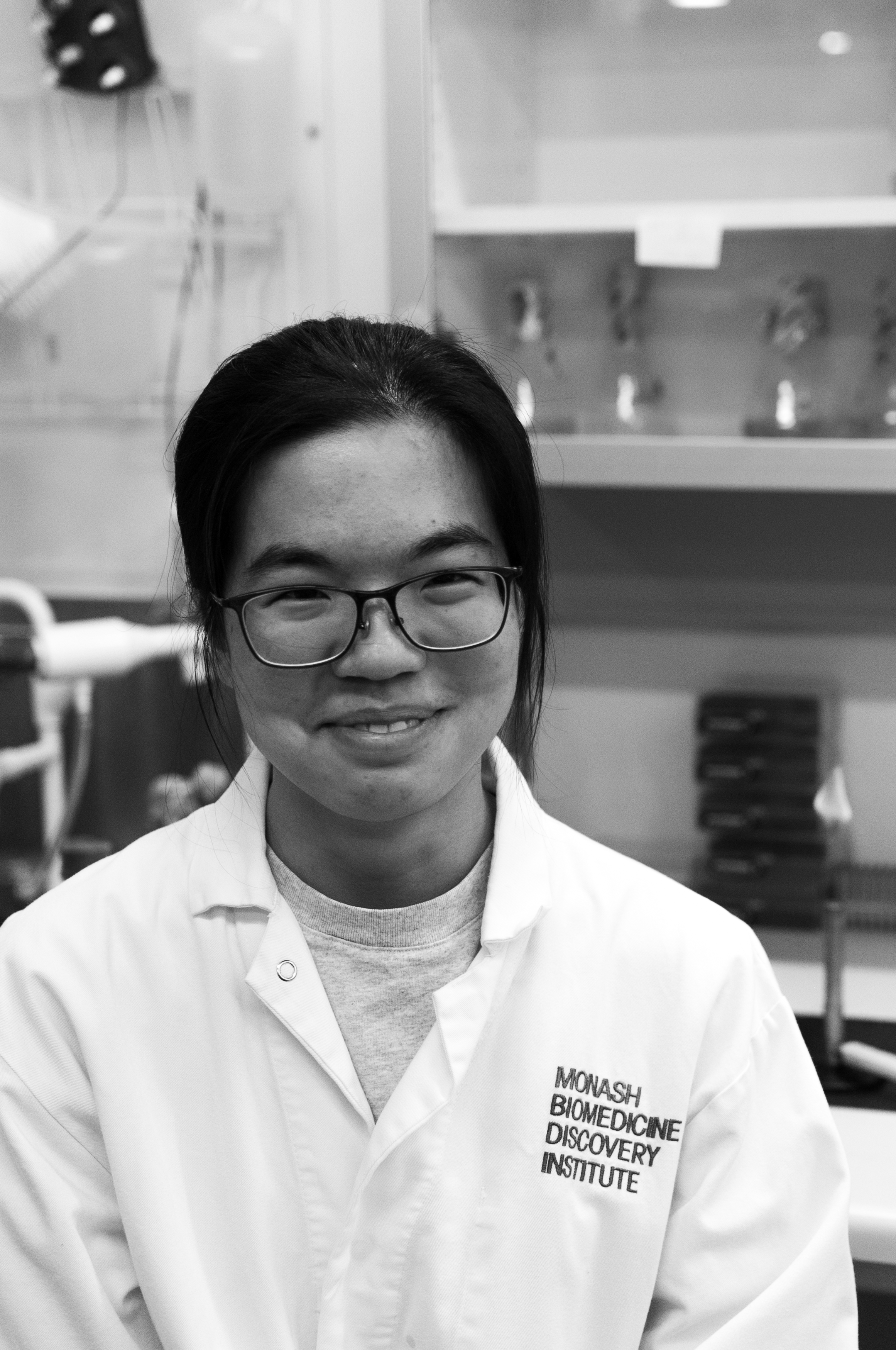 A young woman with shoulder-length dark hair, wearing glasses, and a striped shirt, smiling softly in front of a plain background.