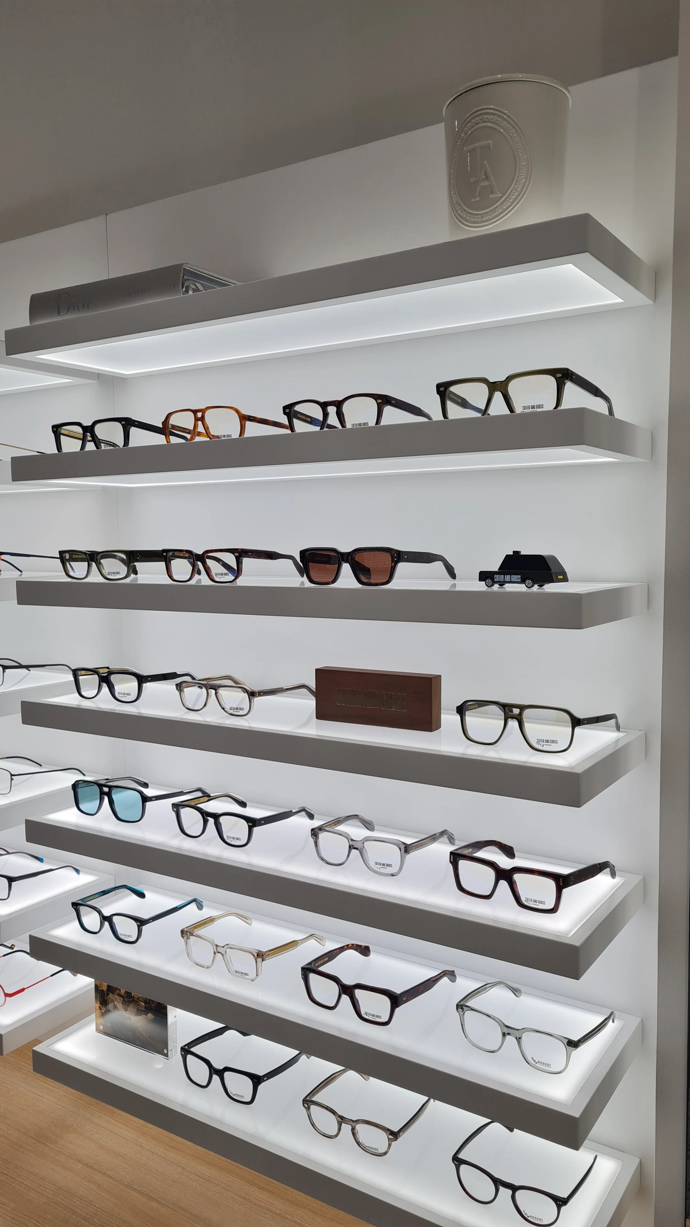 Display of multiple pairs of eyeglasses on white shelves, with bright lighting.
