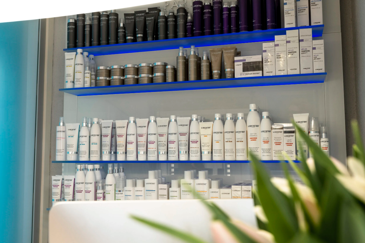 Regale mit verschiedenen Hautpflege- und Haarpflegeprodukten in einer Drogerie oder Kosmetikstudio, hauptsächlich in weißen, braunen und lila Verpackungen.