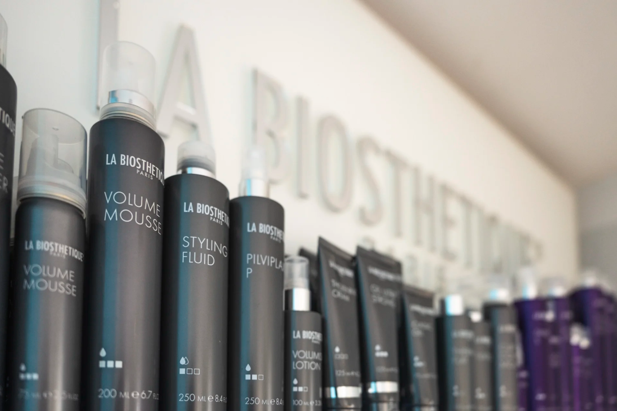 Haarpflegeprodukte auf einem Regal, darunter Volumen Mousse, Styling Fluid, Shampoo und Conditioner.
