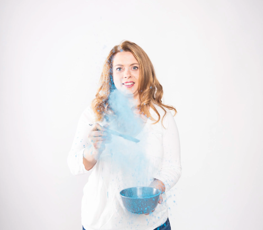 Frau mit rotem Haar, die mit blauer Pulver in einer weißen Umgebung experimentiert.