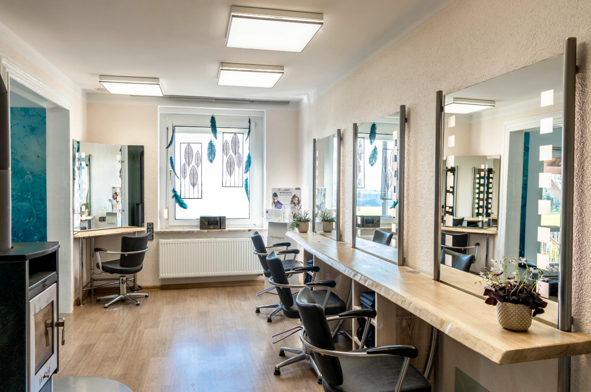 Friseursalon mit Spiegeln, schwarzen Stühlen und Dekorationen an den Fenstern