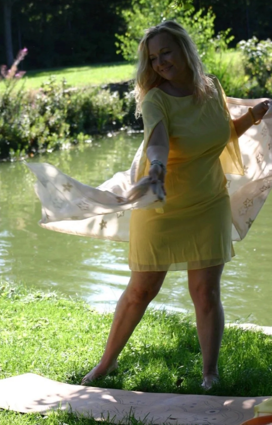 Lächelnde Frau in gelbem Kleid am Flussufer, hält einen Schal
