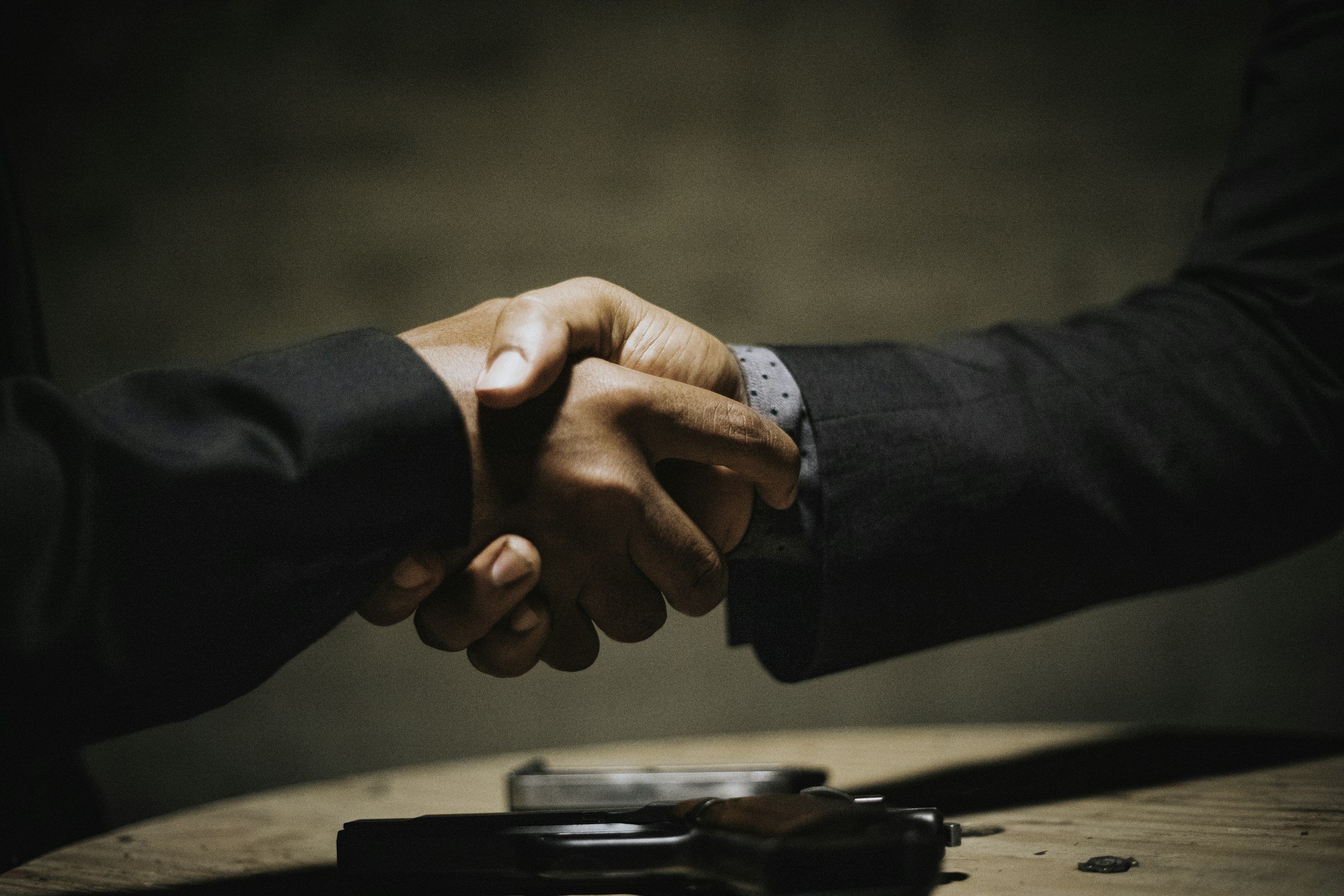 Two people in business attire shaking hands, with one person's right hand grasping the other's right hand over a table.