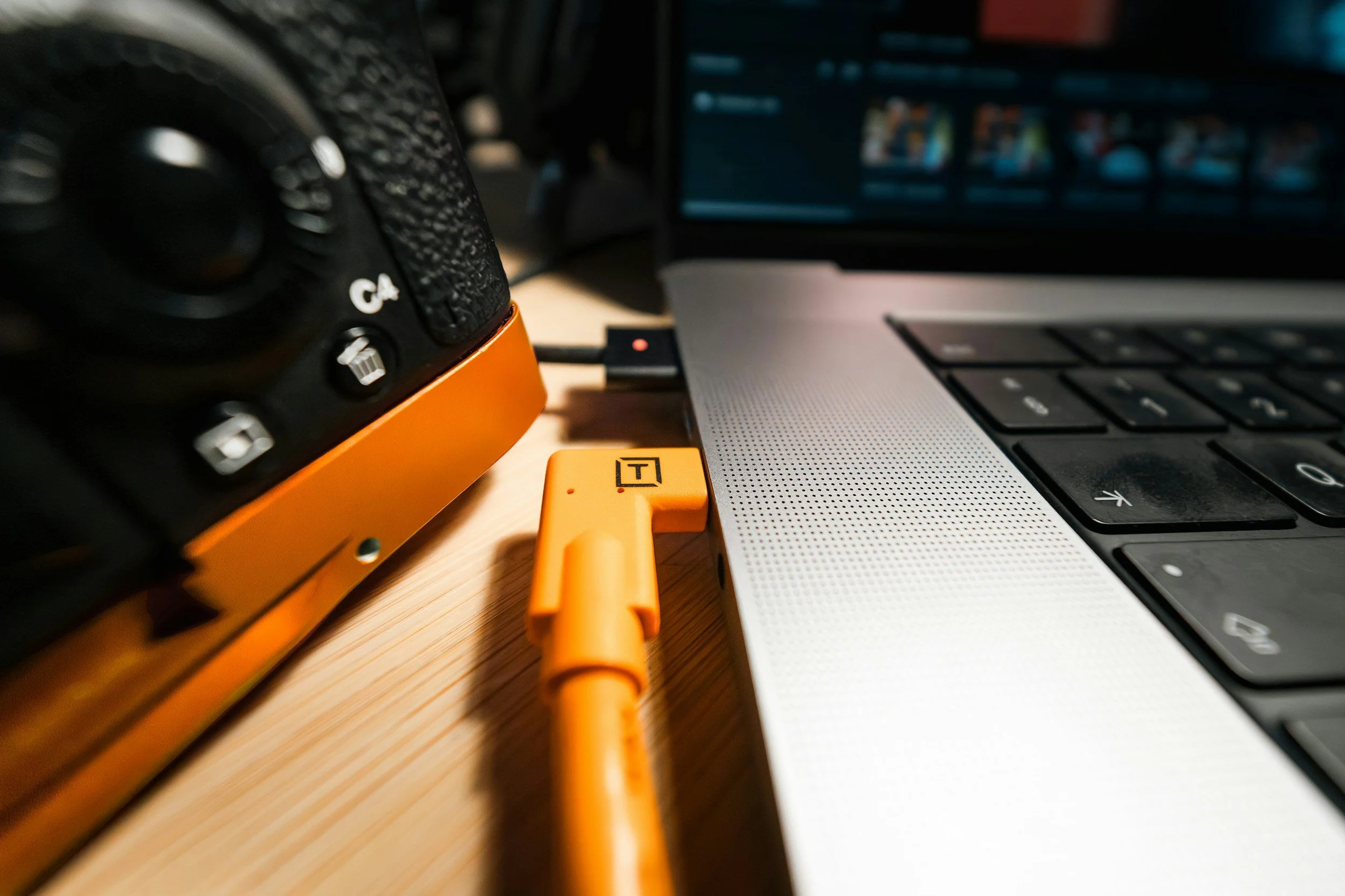 Close-up of a computer laptop keyboard, orange USB-C cable plugged into a device, with a black speaker and yellow USB stick nearby.